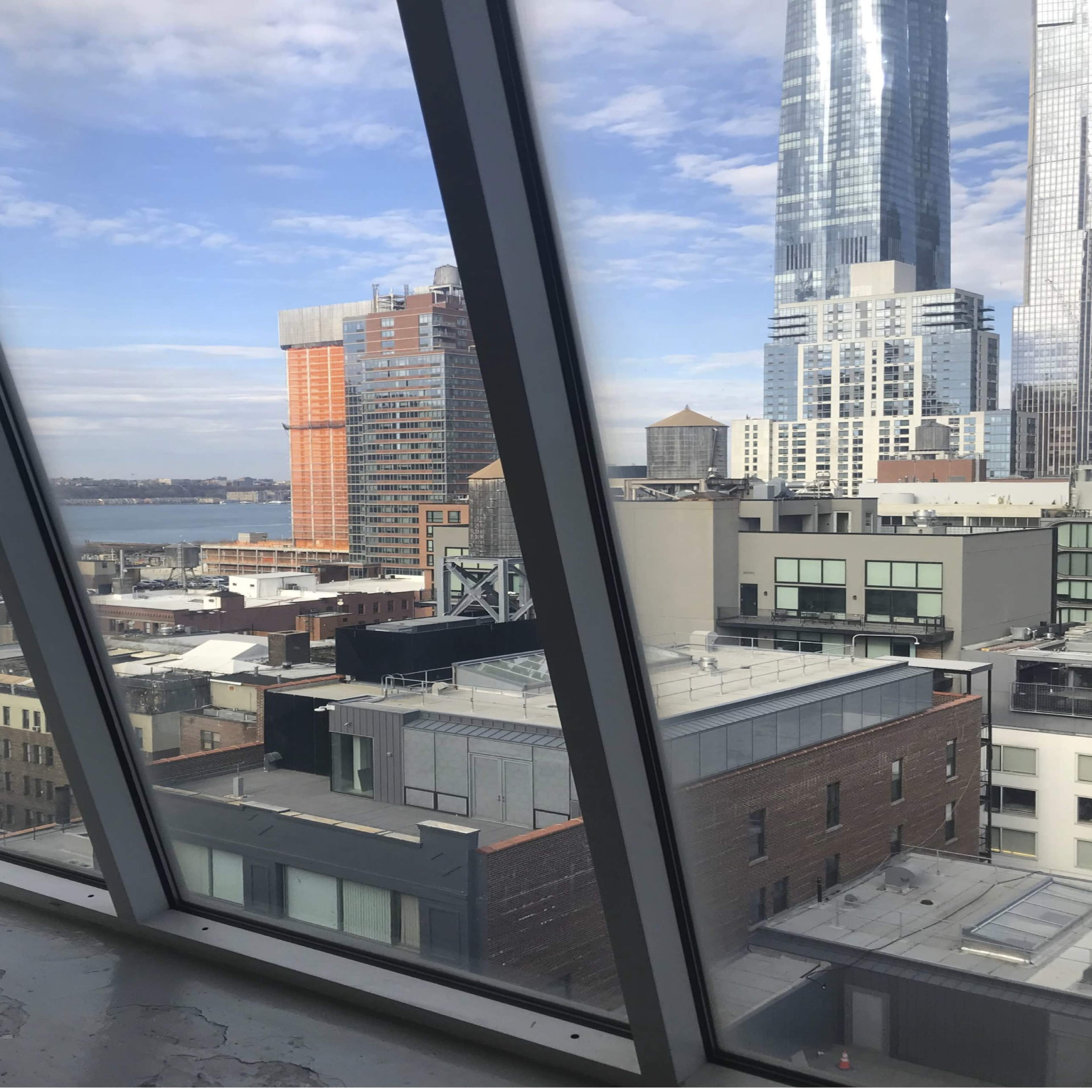 A view through large, angled windows overlooking a cityscape with various buildings and a body of water in the background.