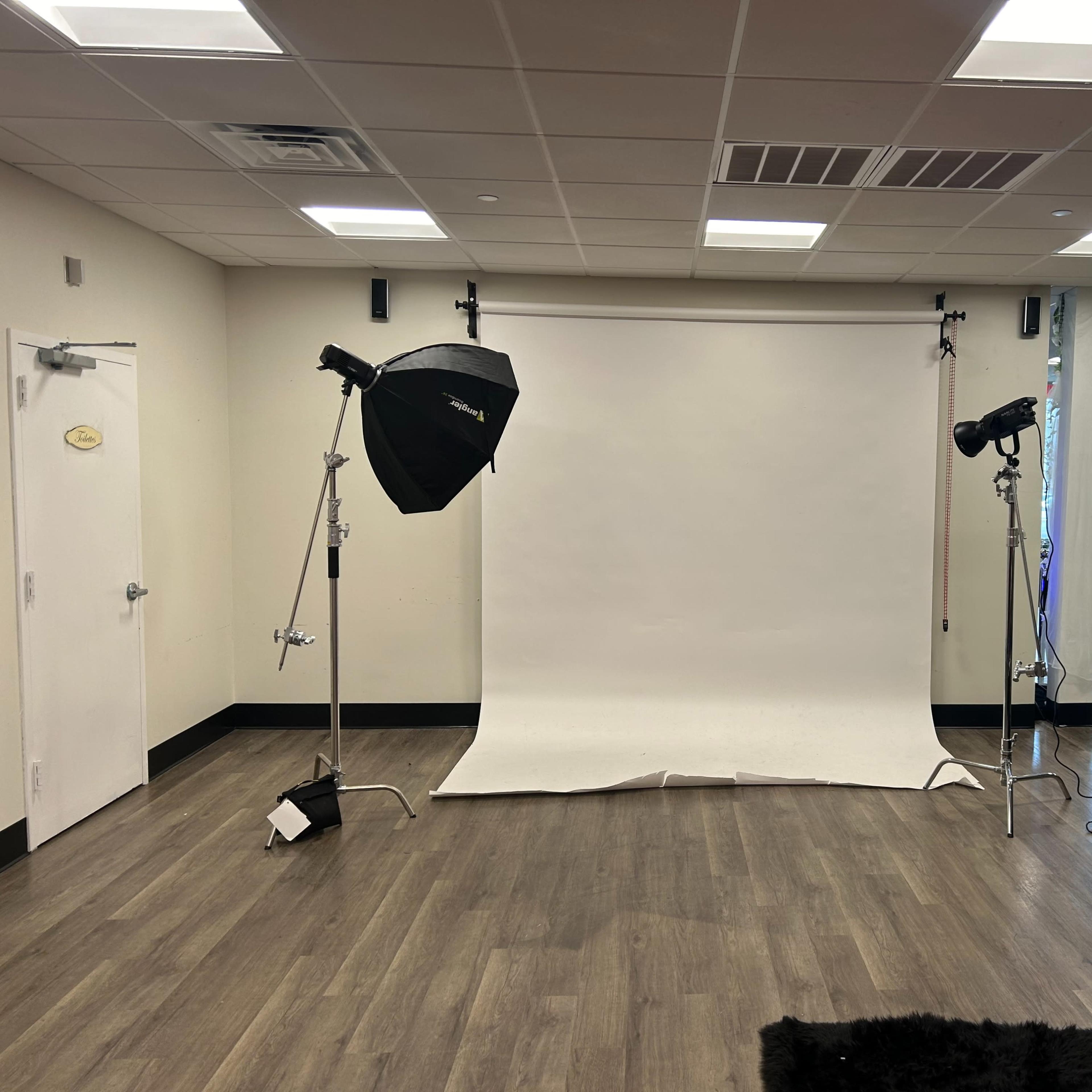 A photography studio setup featuring a white backdrop and two lights with softboxes positioned on either side.