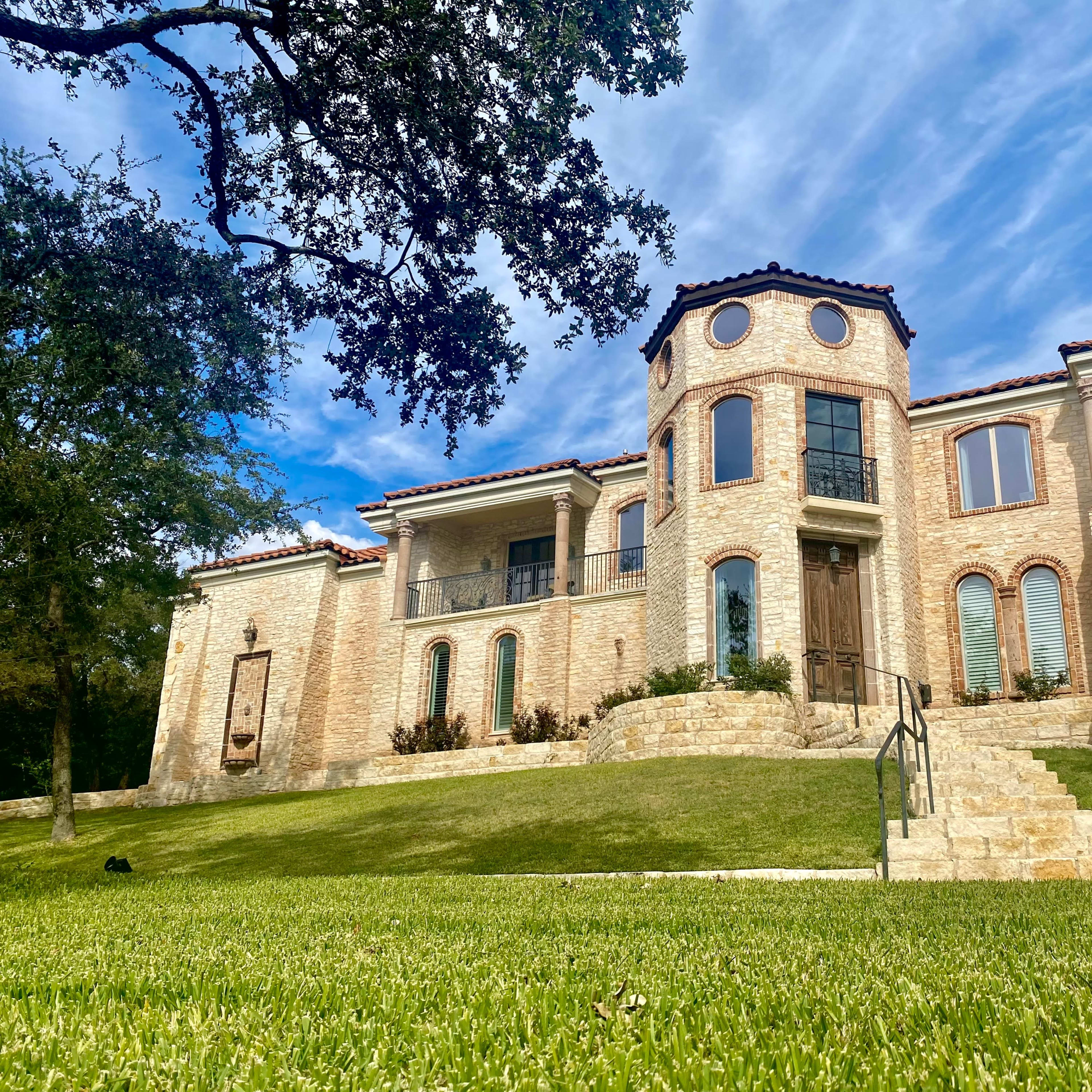 A large, two-story stone house with multiple circular windows is set on a grassy slope.