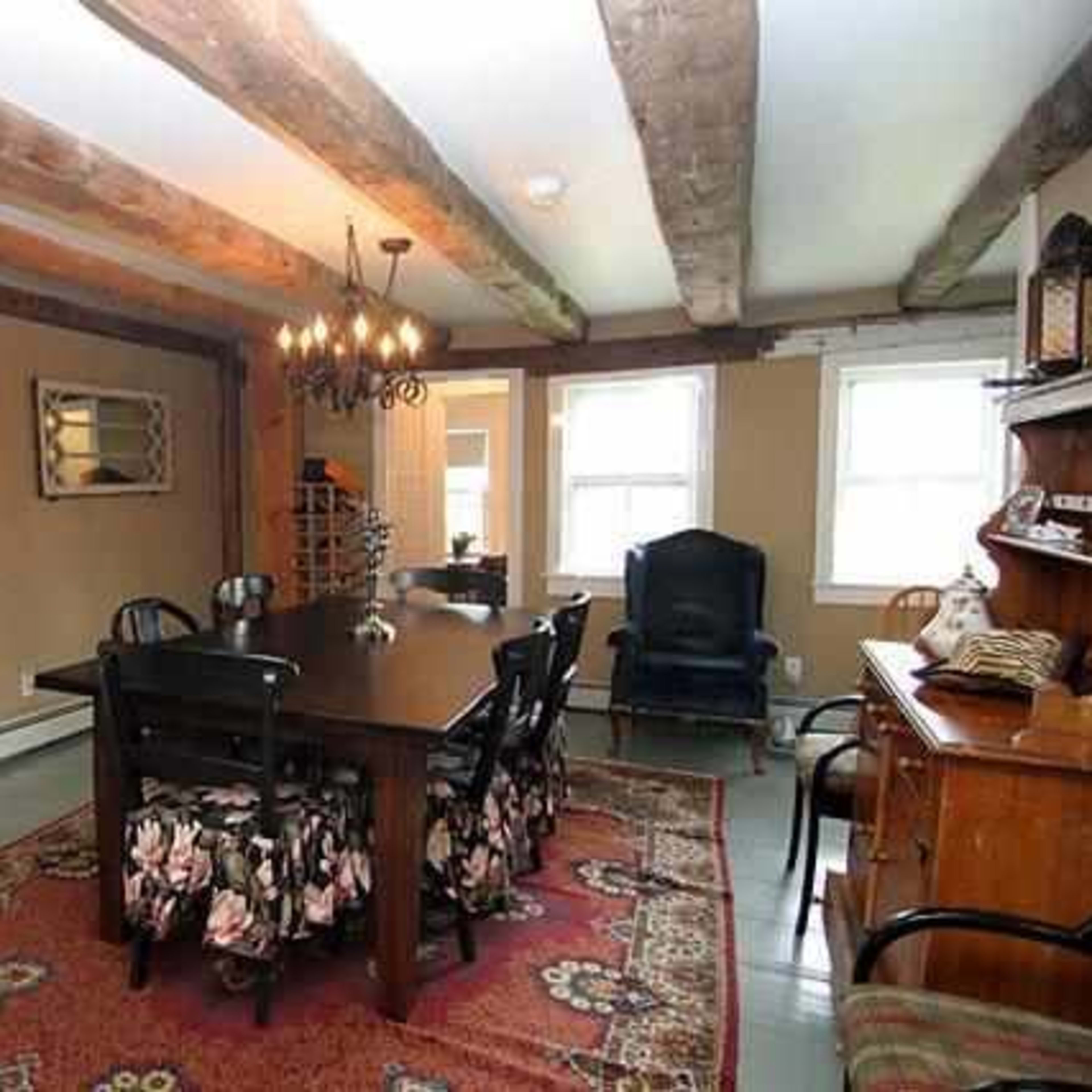 A rustic dining room with a large wooden table surrounded by black chairs, a chandelier overhead, and exposed wooden beams on the ceiling.