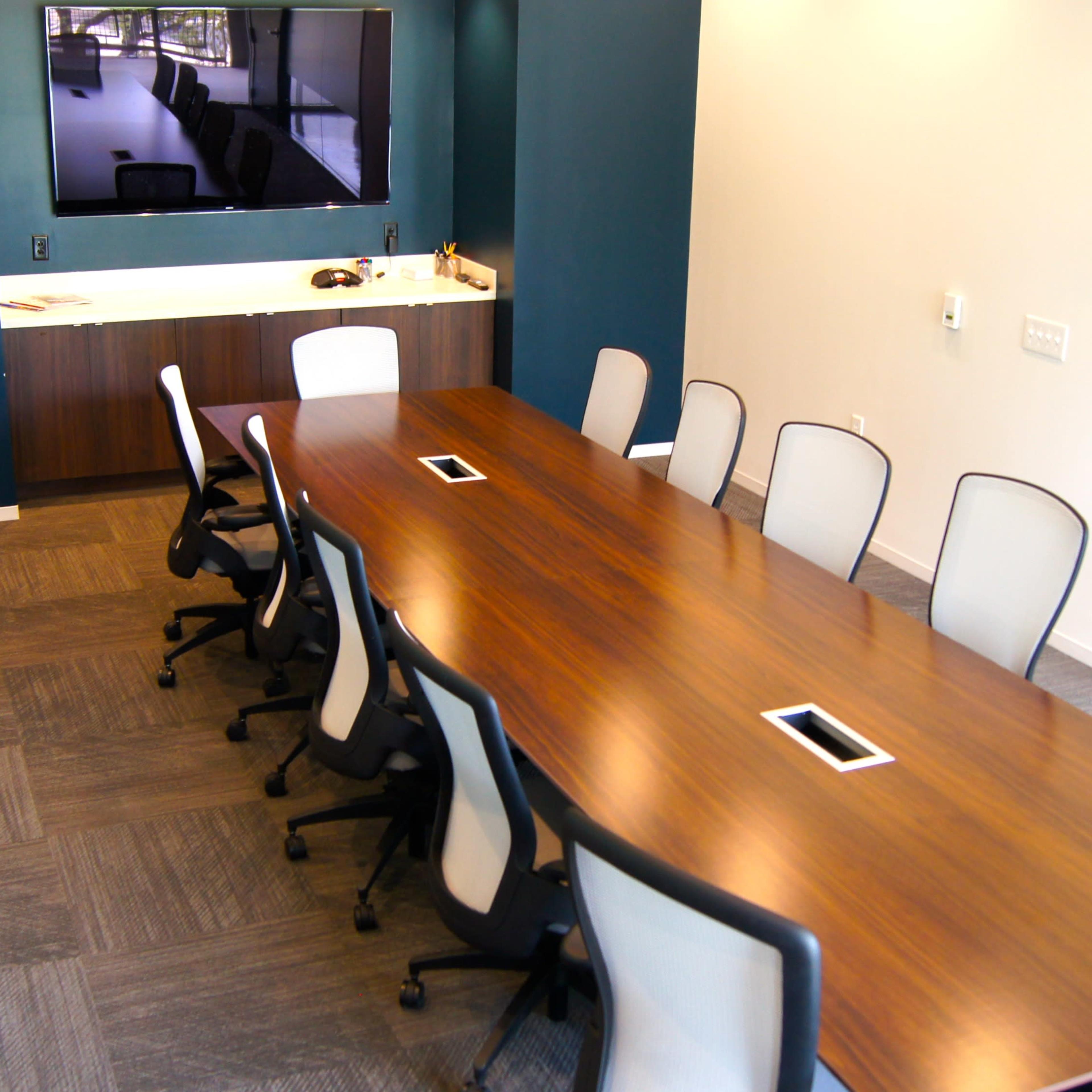 A modern conference room with a long wooden table and several ergonomic chairs arranged around it.