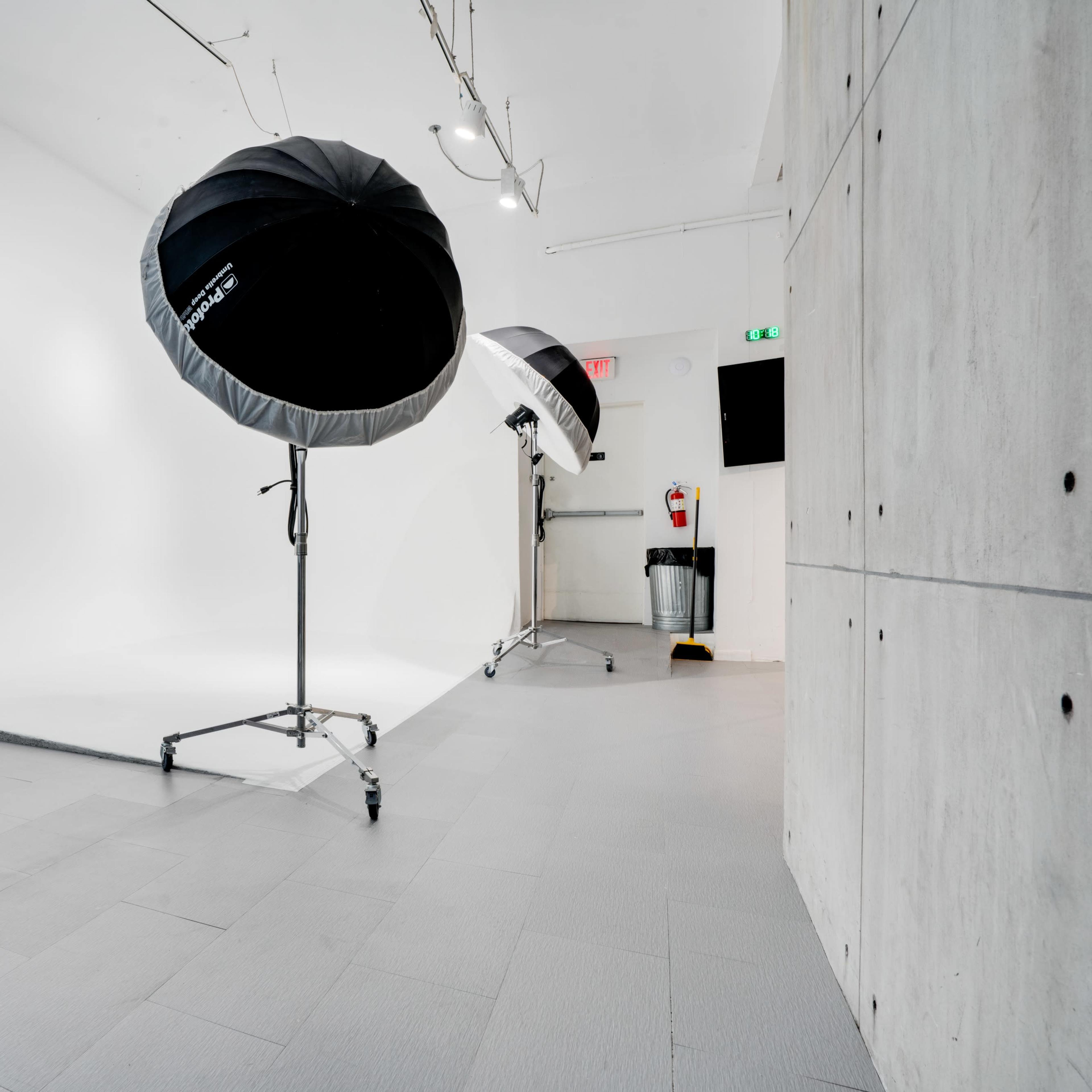 A photography studio with large softbox lights, a mirror, and a minimalistic setup featuring a gray floor and white backdrop.