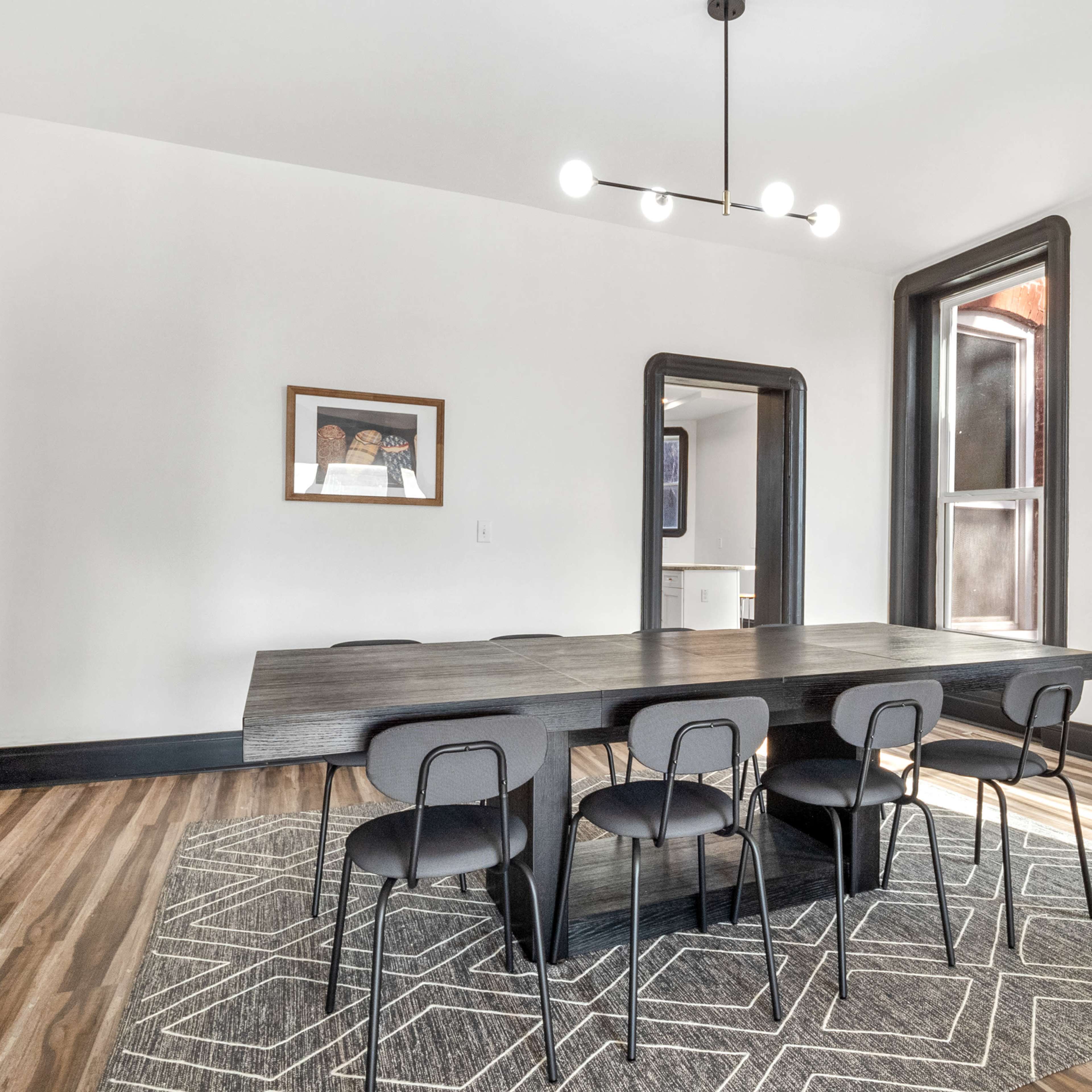 A modern dining room features a rectangular table surrounded by six black chairs, with large windows and minimalist decor.