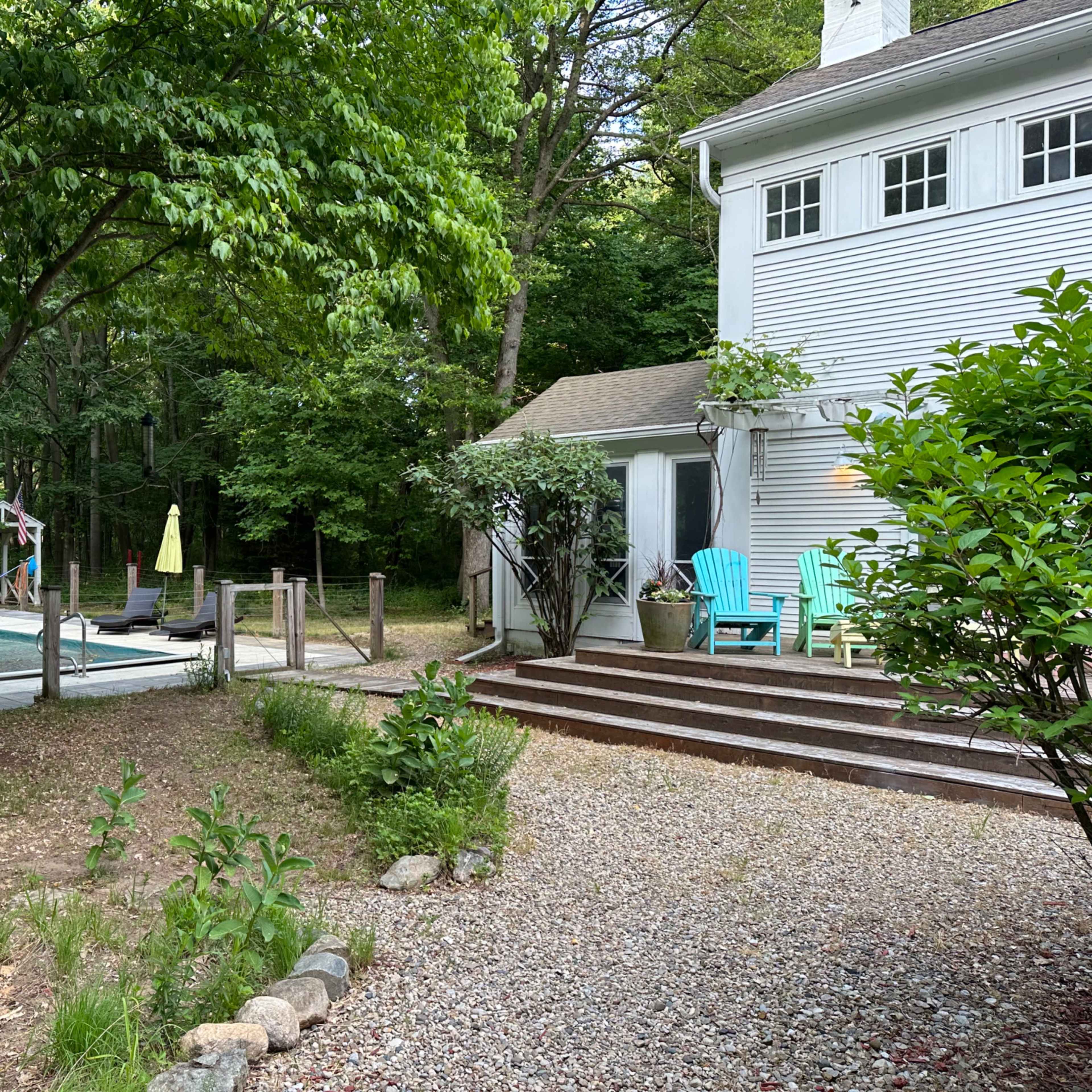 A backyard area with a pool, lounge chairs, and steps leading up to a white house surrounded by greenery.