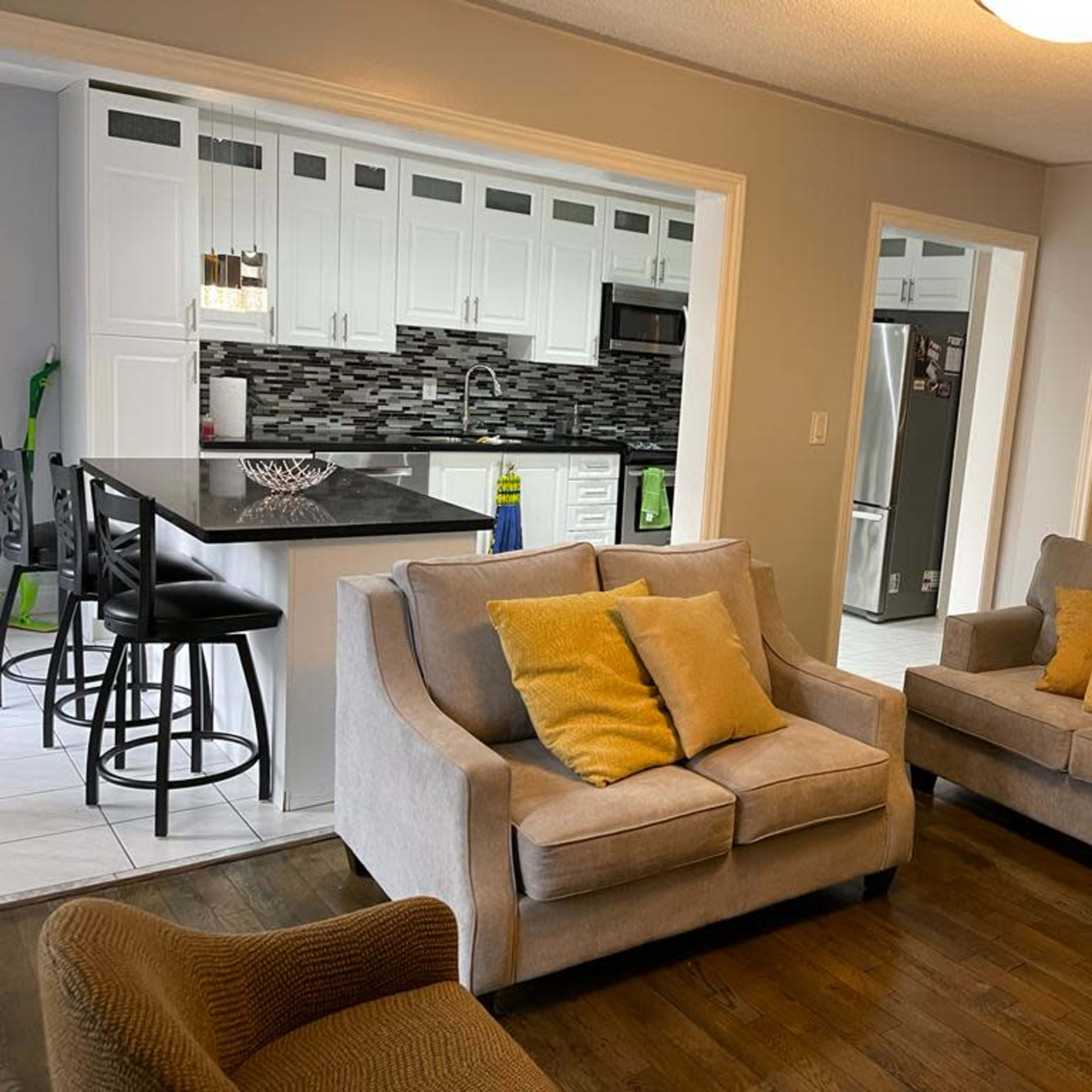 A living room with two gray sofas, a coffee table, and an open kitchen area in the background featuring white cabinetry and a black countertop.