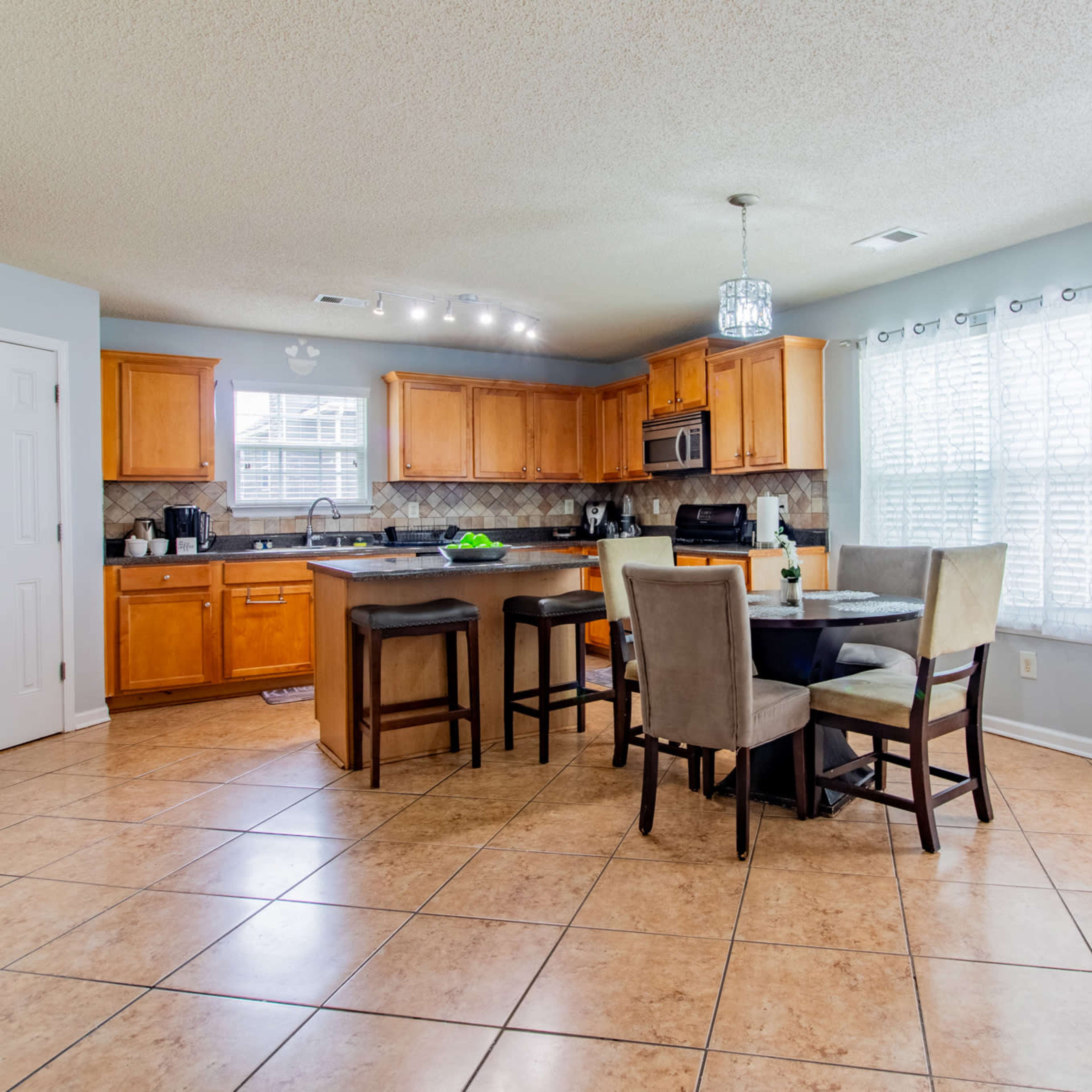 A spacious kitchen with wooden cabinets, a large island, and a dining area featuring a round table and four chairs.