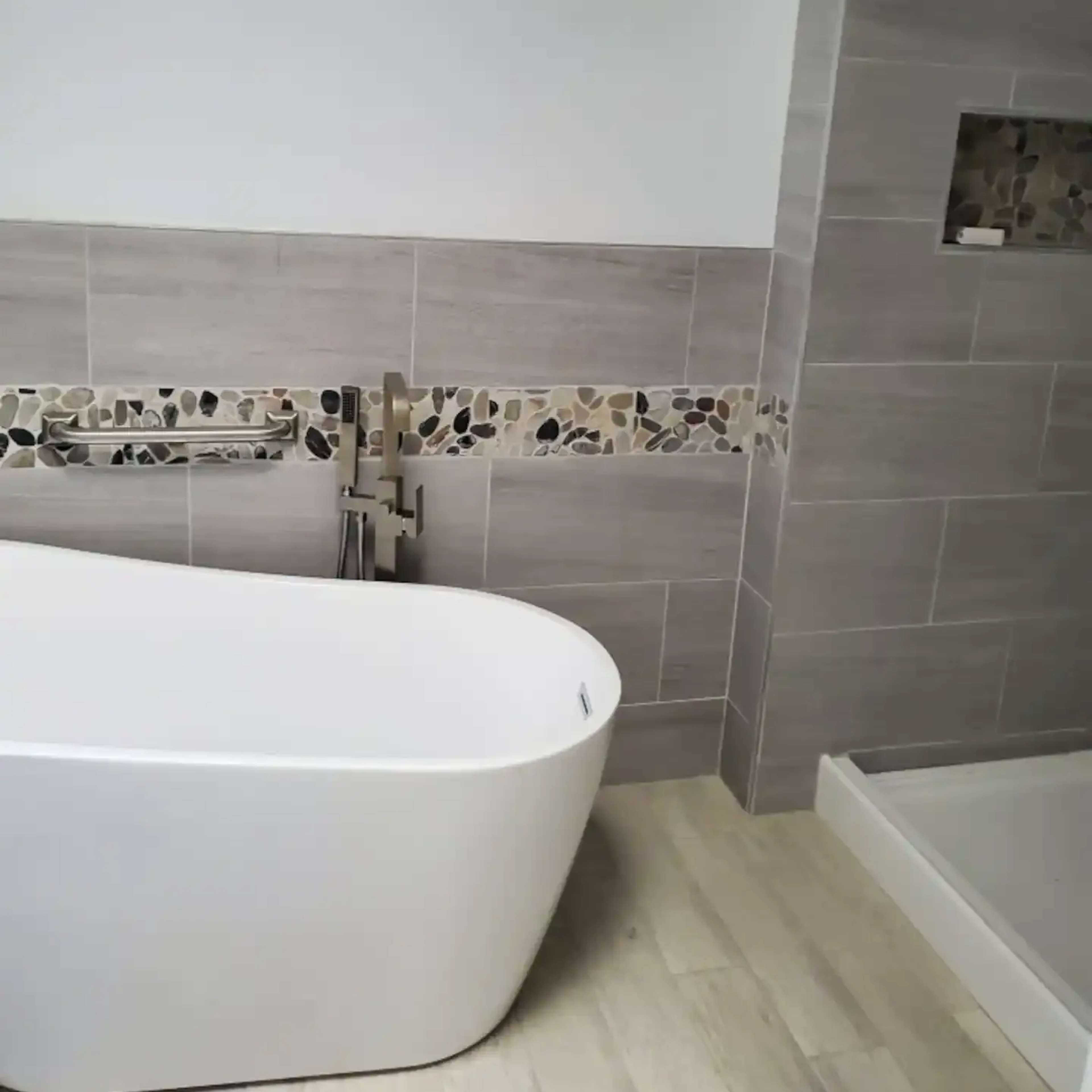 A modern bathroom with a freestanding white bathtub, a decorative tile border, and a shower area with a glass door.