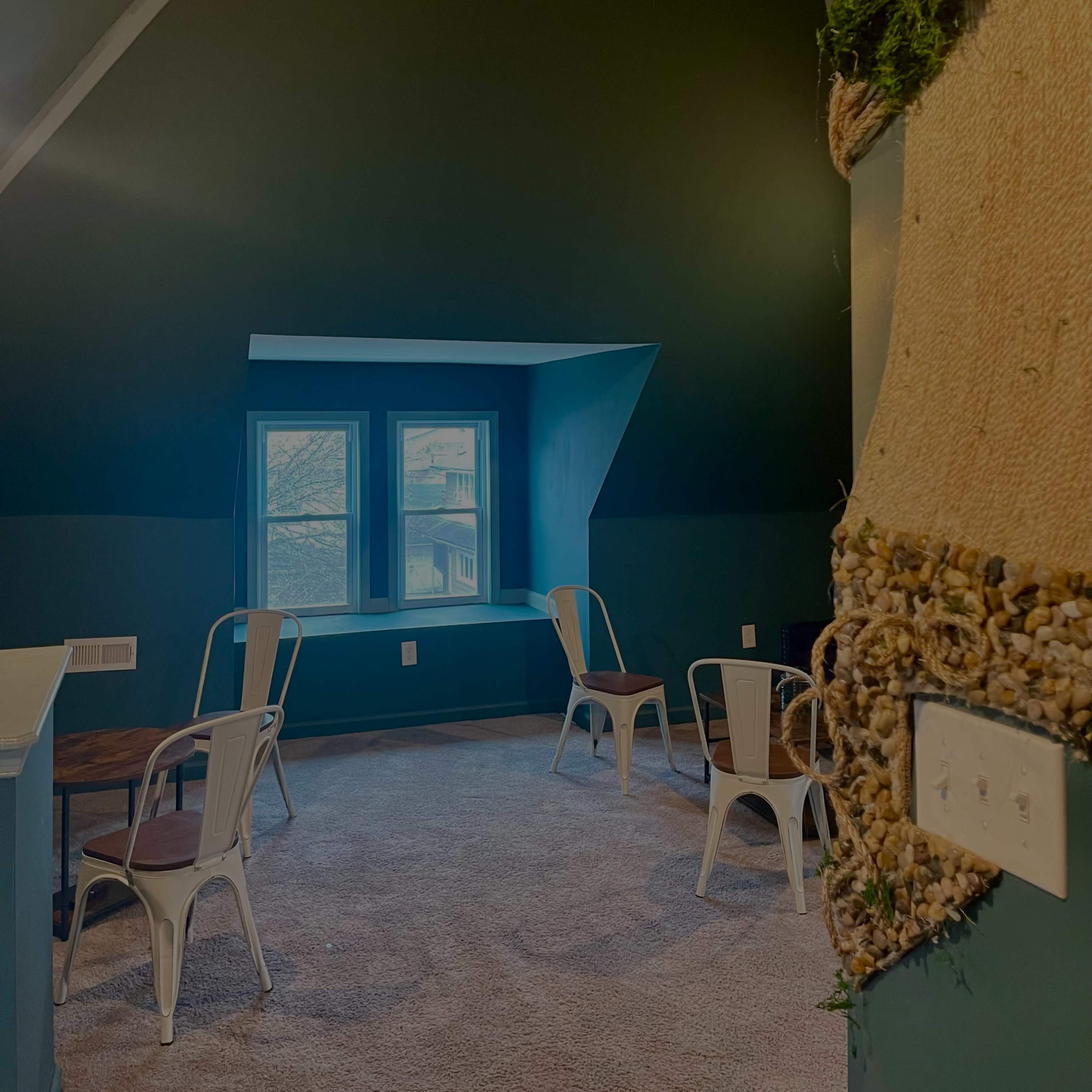 A small room with green walls, a carpeted floor, two metal chairs, a wooden table, and a large window that overlooks the outside.