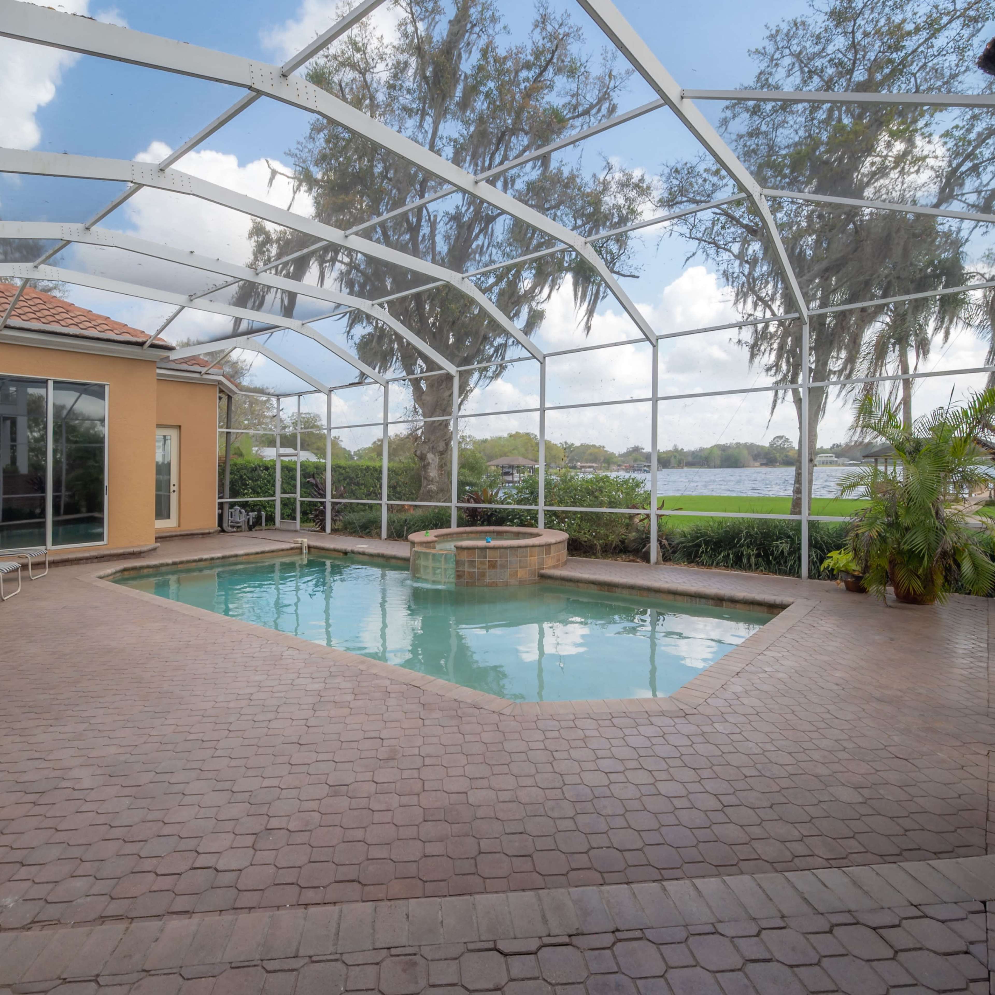 A screened-in patio area with a swimming pool and a spa, surrounded by greenery and open water views.