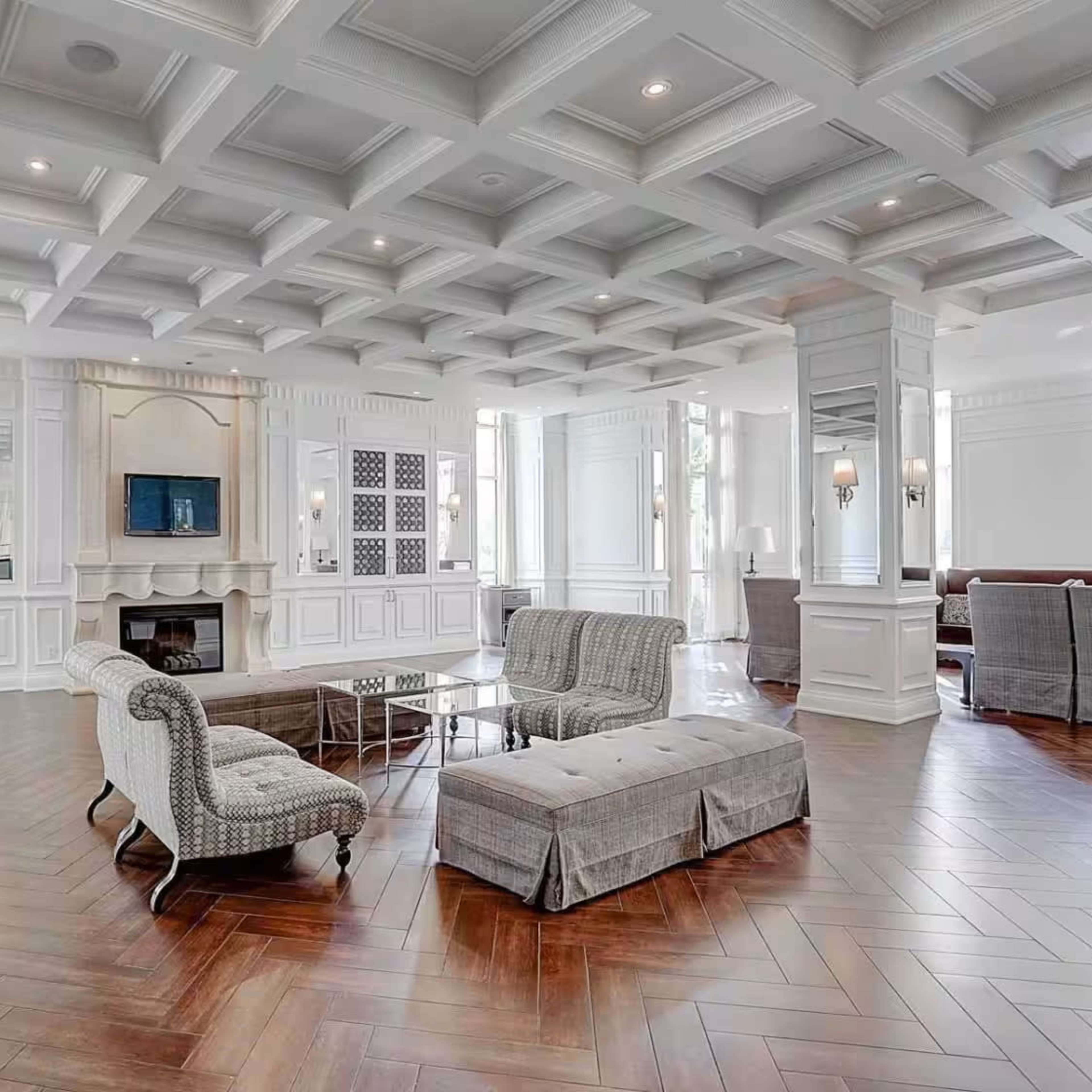 The room features a spacious layout with a coffered ceiling, hardwood flooring, and comfortable seating arrangements around a central coffee table.