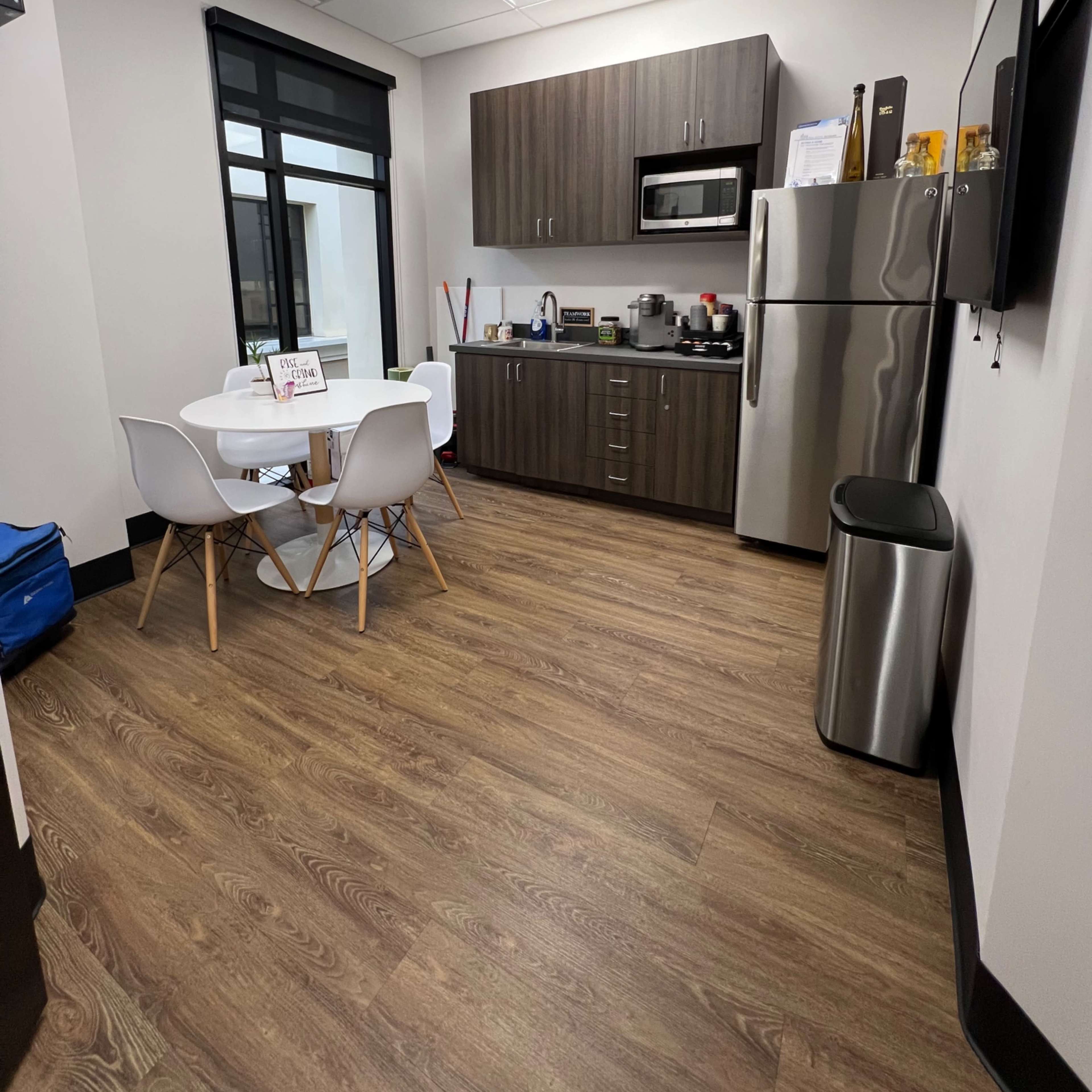 A modern kitchenette features a table with four chairs, a microwave, a refrigerator, and cabinetry along one wall.