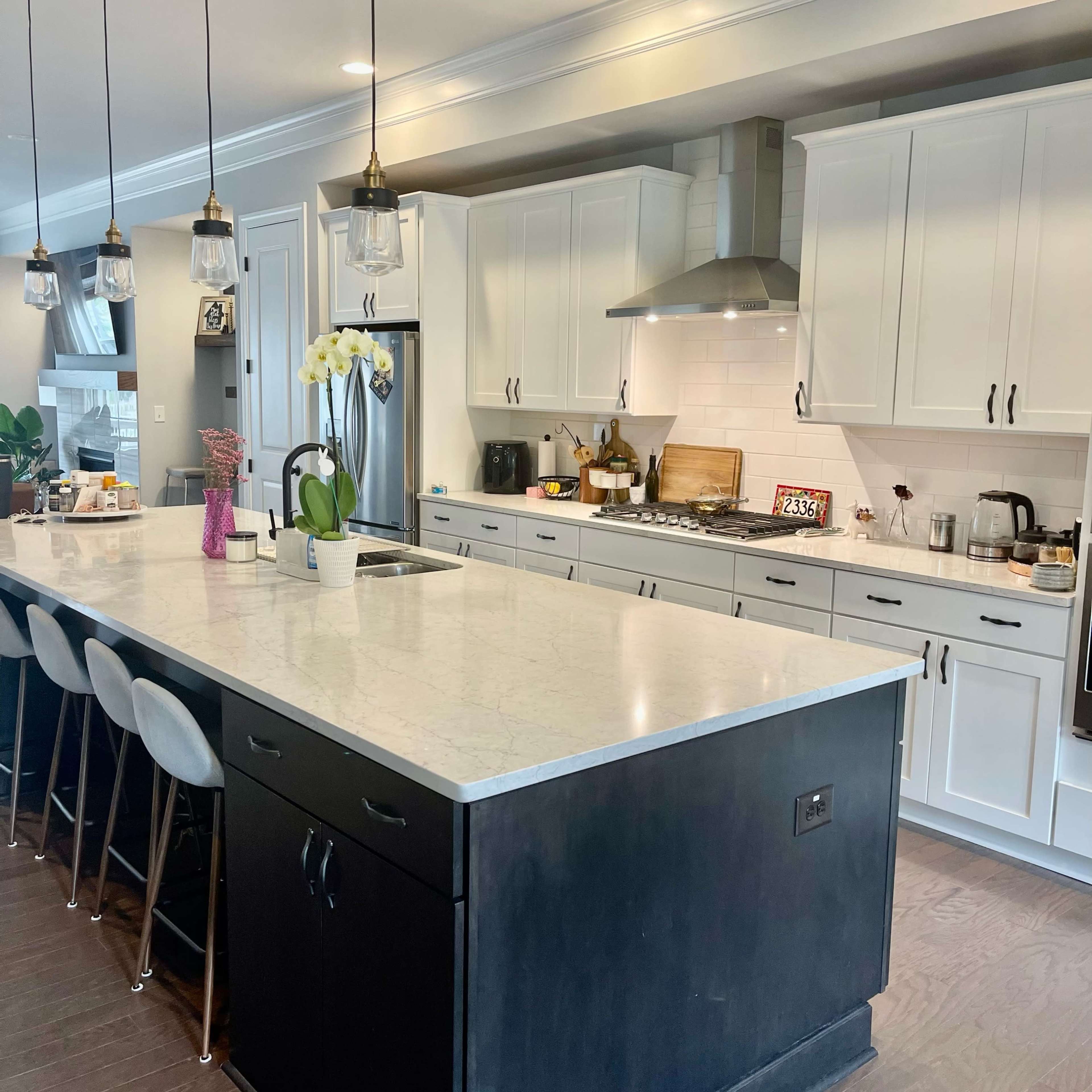 A modern kitchen features a large island with bar seating, white cabinets, and stainless steel appliances.