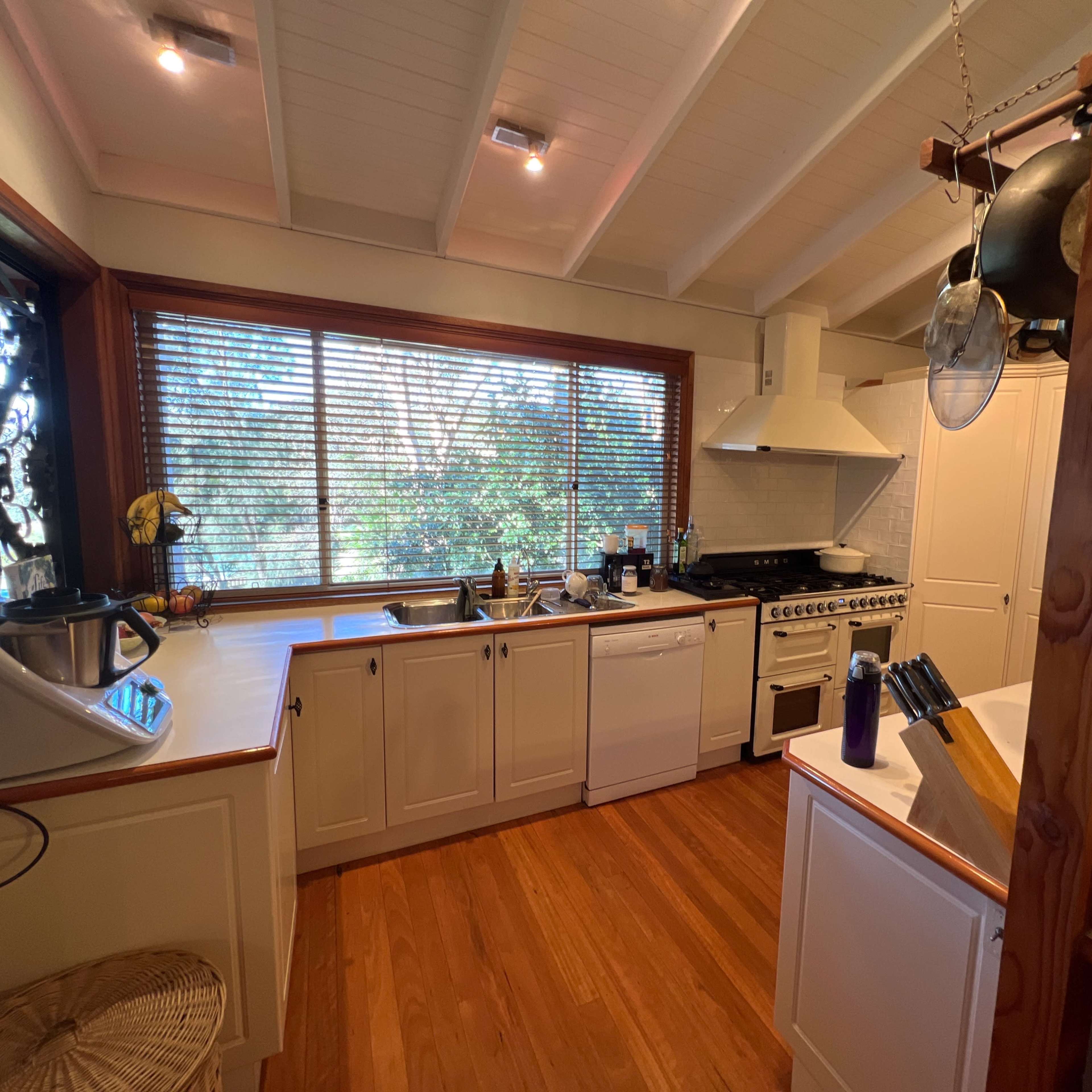 A kitchen features white cabinets, a dishwasher, a stove, and large windows overlooking greenery.