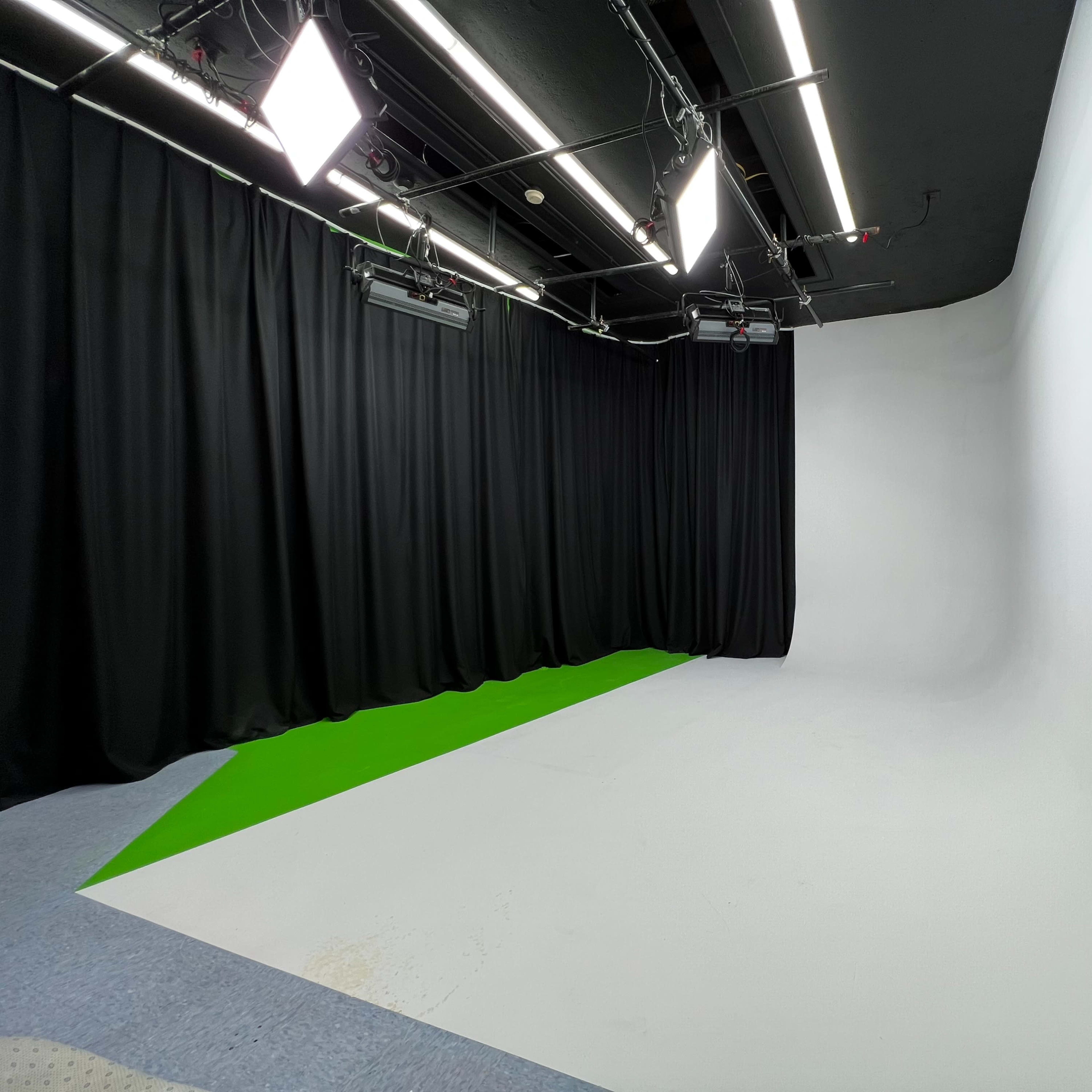 A photo studio with a seamless white backdrop, green flooring, and black curtains.