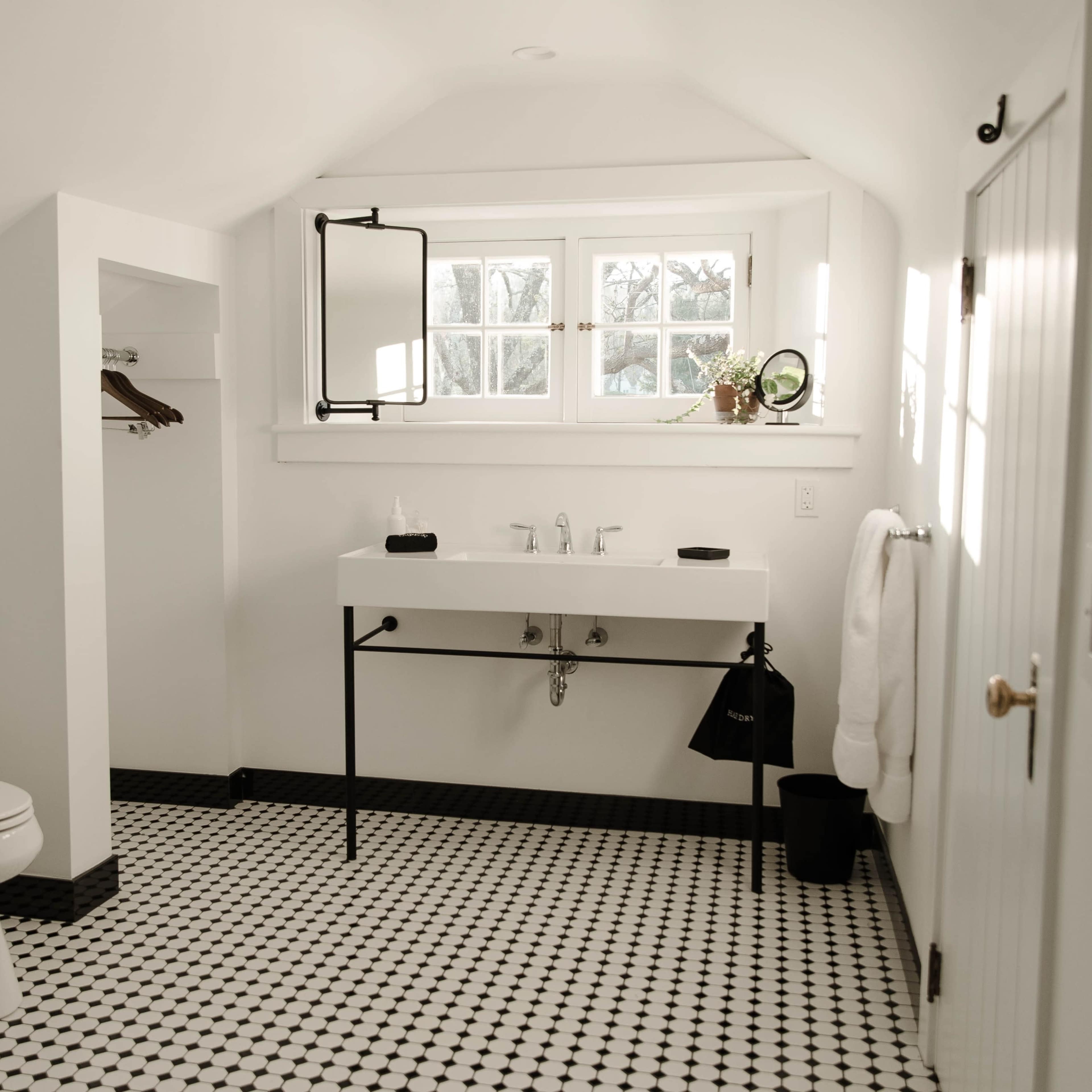 A clean, modern bathroom featuring a white sink, black and white tiled floor, and natural light from a window.