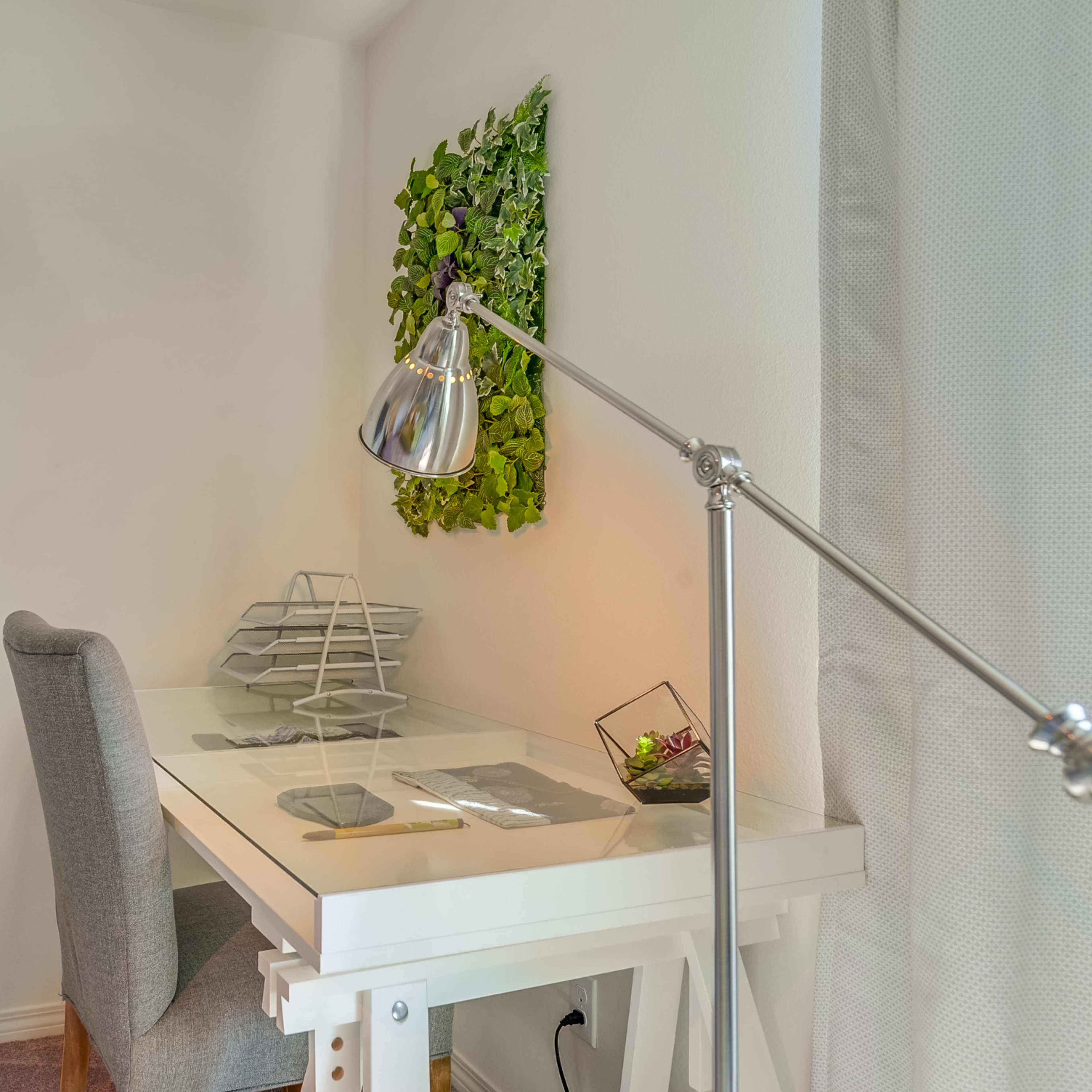 A minimalist workspace featuring a clear desk, a gray chair, a modern desk lamp, and a small vertical garden on the wall.