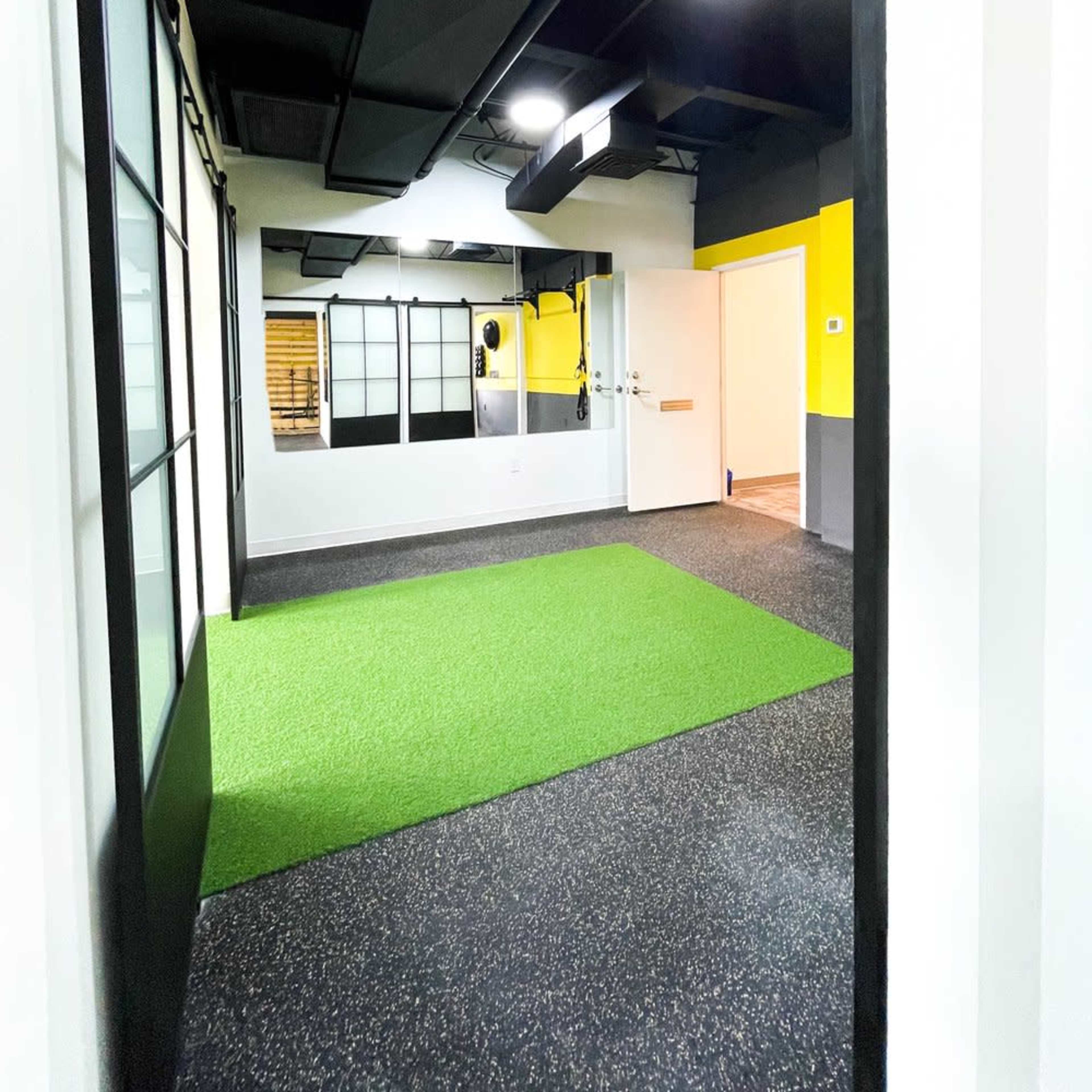 A fitness studio with green turf flooring, black and yellow walls, and large windows.