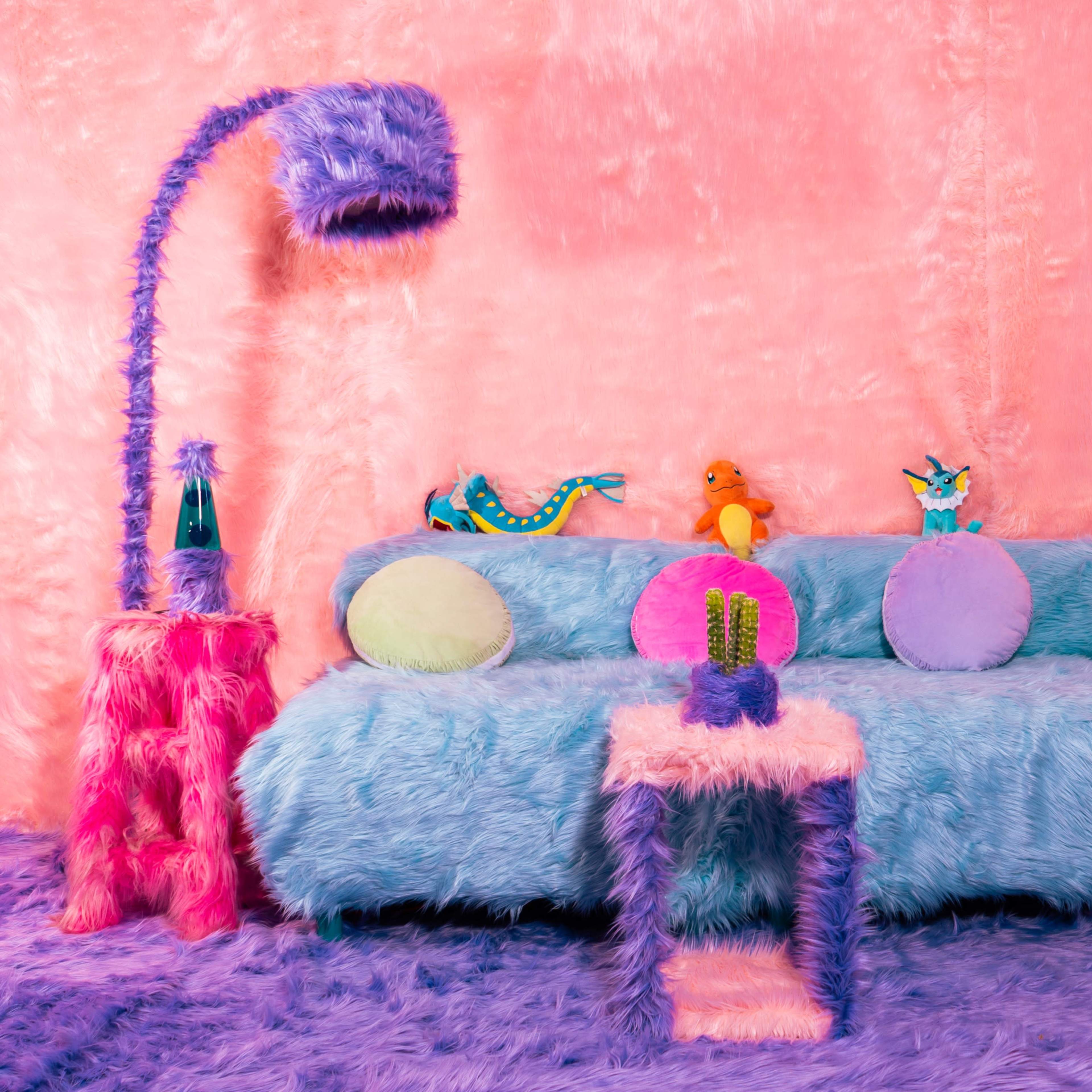 The scene features a fluffy, pastel-colored living room with a light blue sofa adorned with colorful round pillows, accompanied by playful plush toys and a pink lamp.