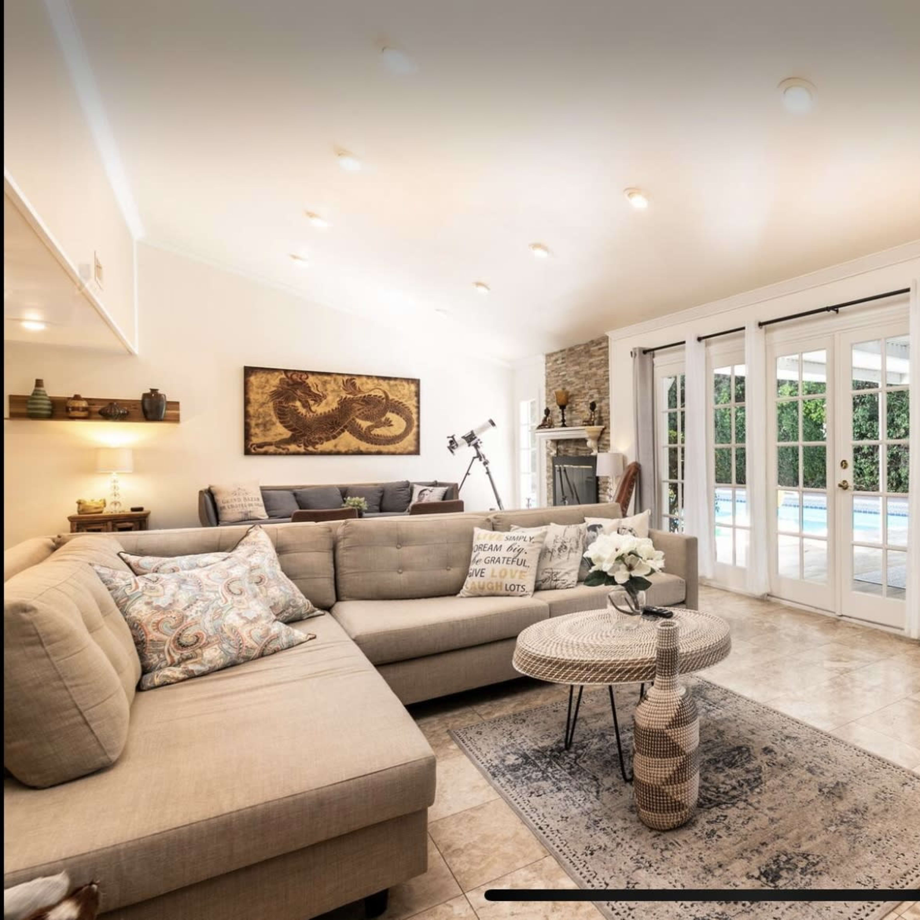 A bright living room with a sectional sofa, a round coffee table, and large glass doors leading to an outdoor pool area.