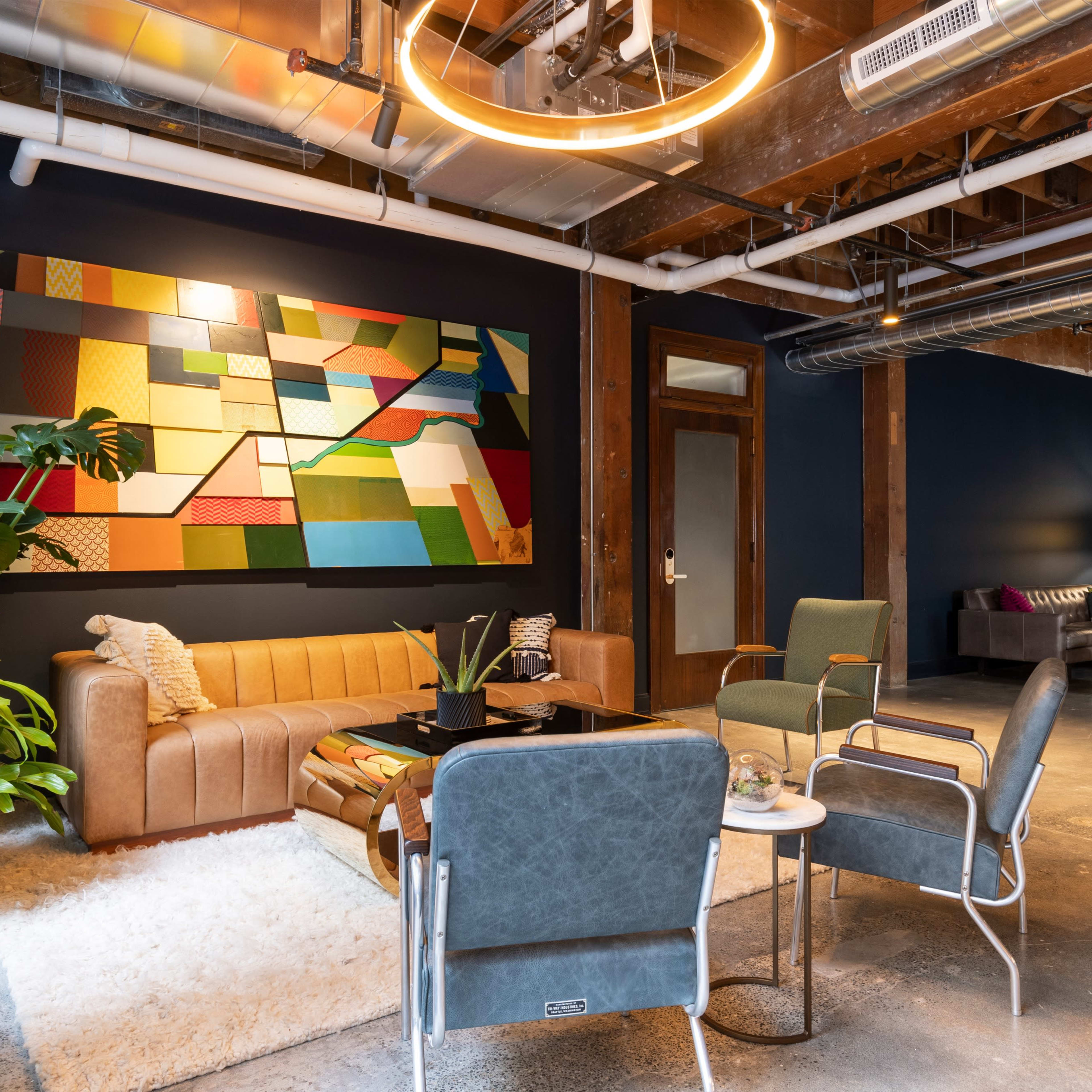 A modern, multi-functional lounge area featuring a brown sofa, potted plants, a large abstract painting on the wall, and a mix of seating options including armchairs and small tables.