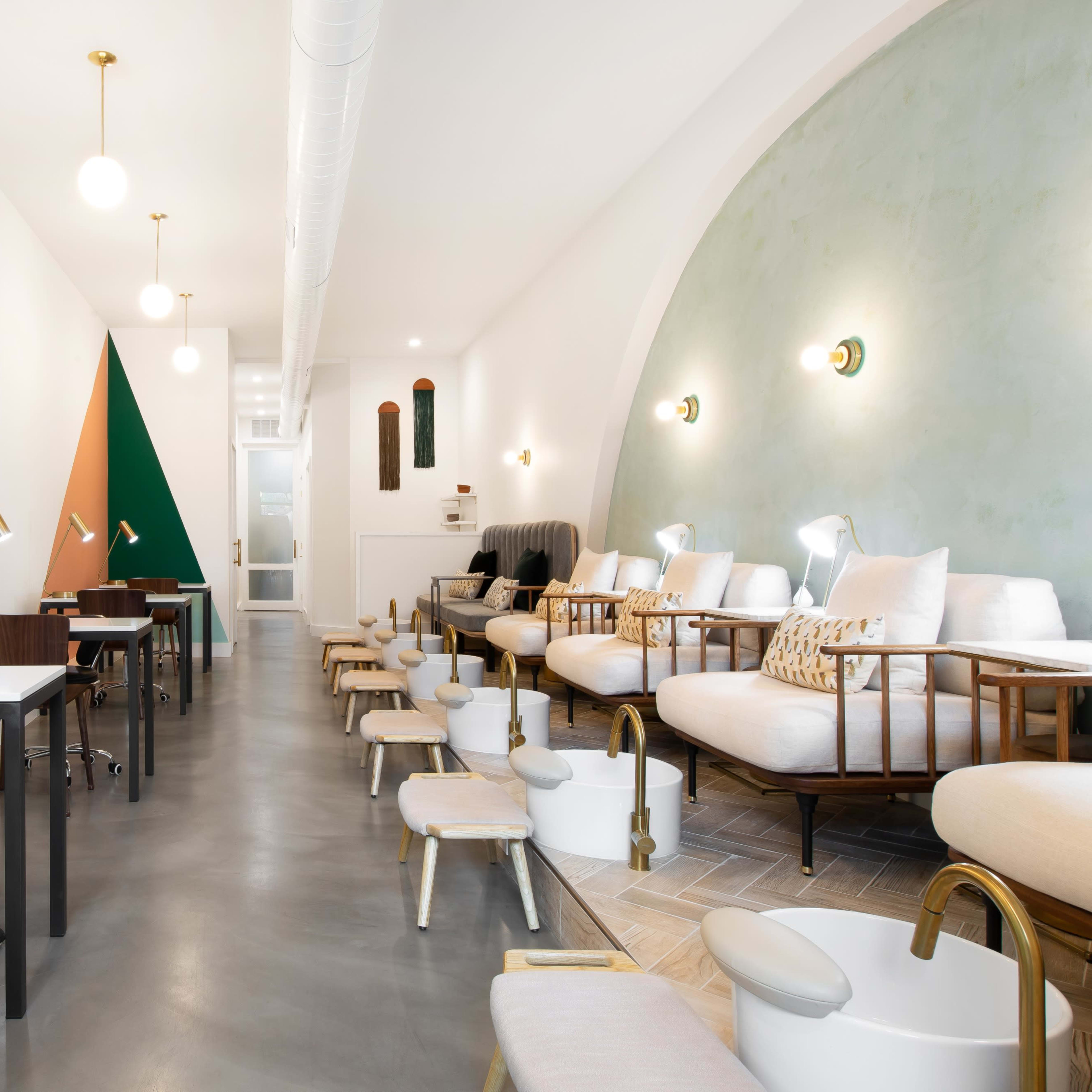 A modern salon interior featuring several workstations, comfortable seating, and a stylish color scheme with green and orange accents.