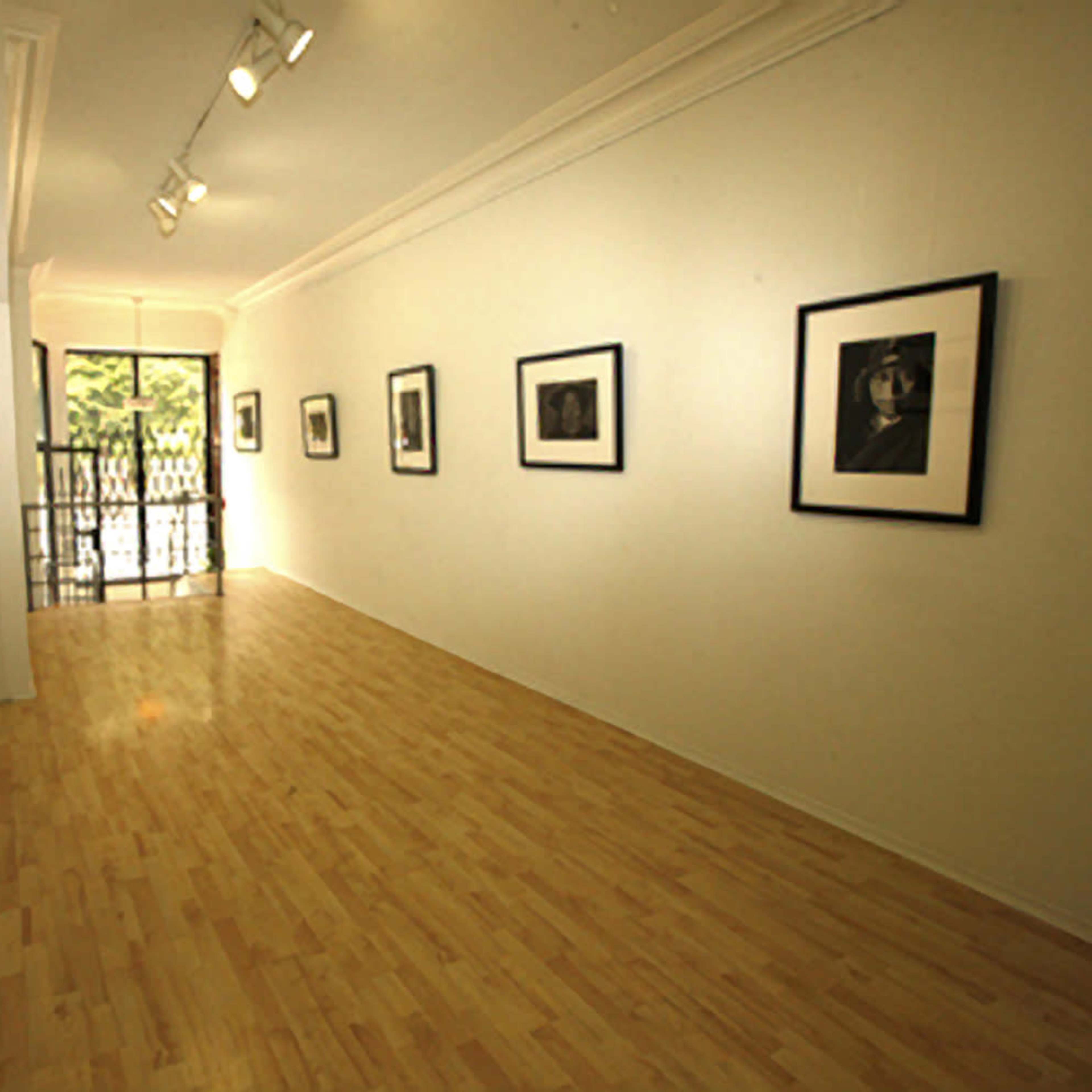A well-lit art gallery featuring several framed photographs displayed on the white walls, with a door leading to an outdoor area.