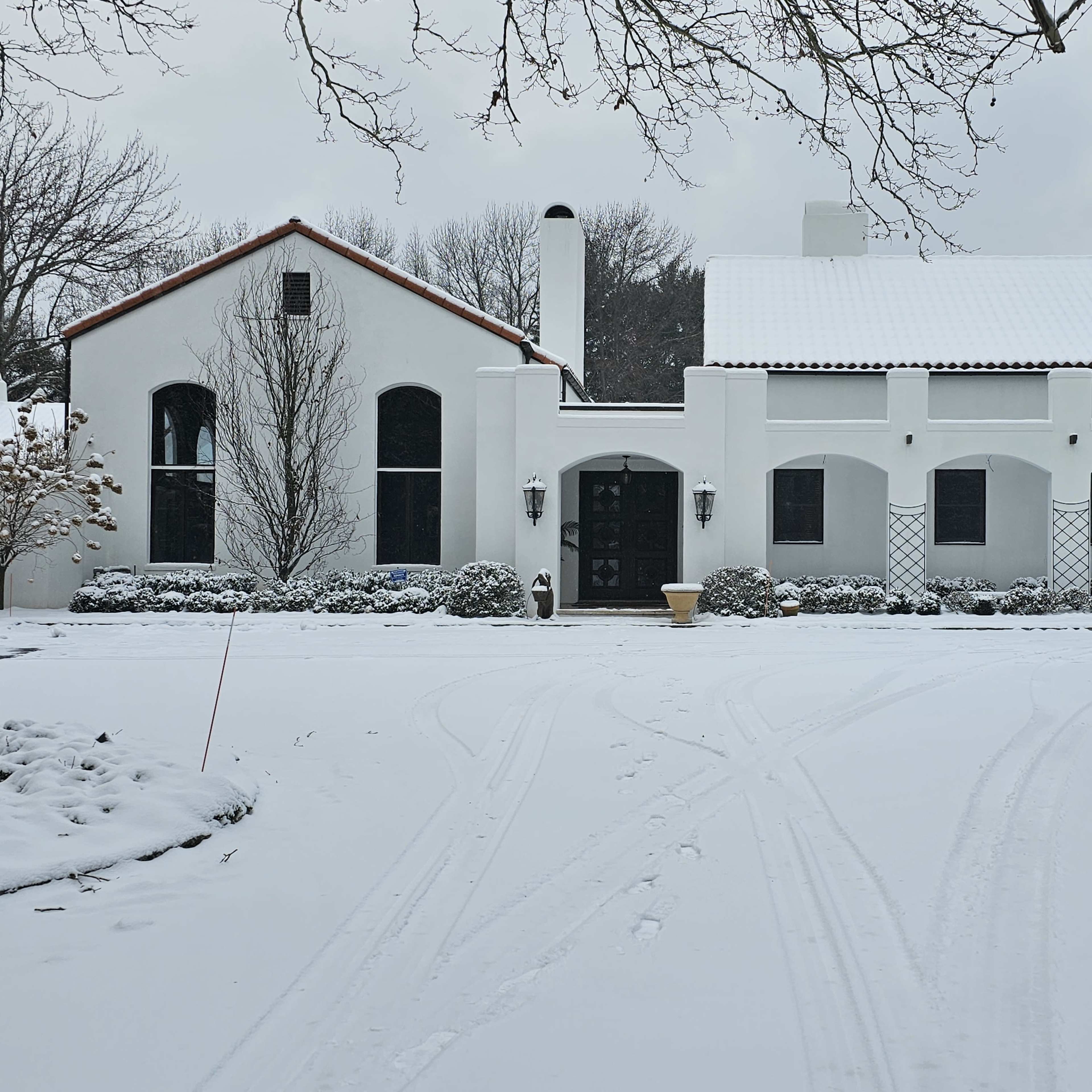 A white stucco house with a red-tiled roof is set against a snowy landscape.