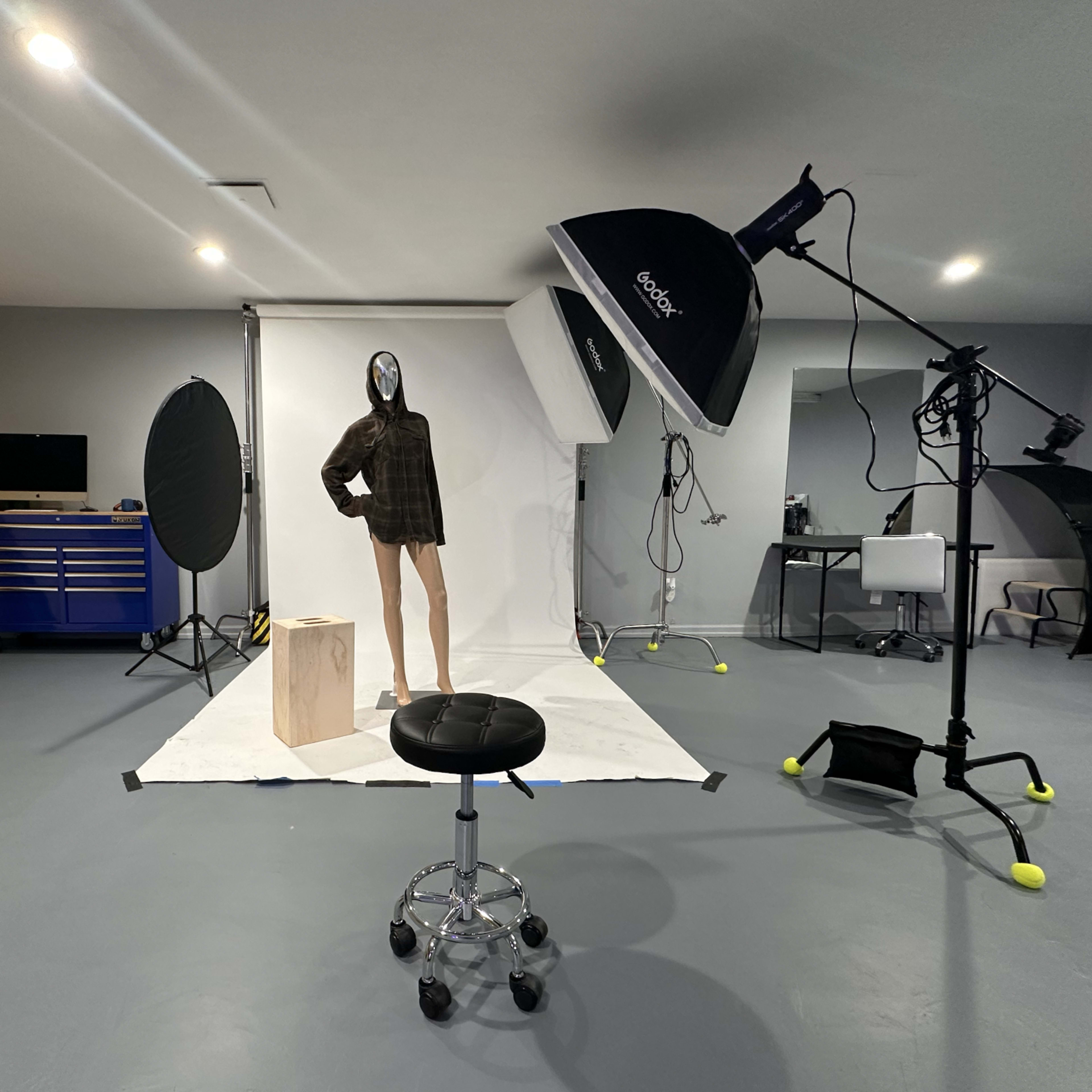 A photography studio with a mannequin wearing a shirt, a backdrop setup, and various lighting equipment.