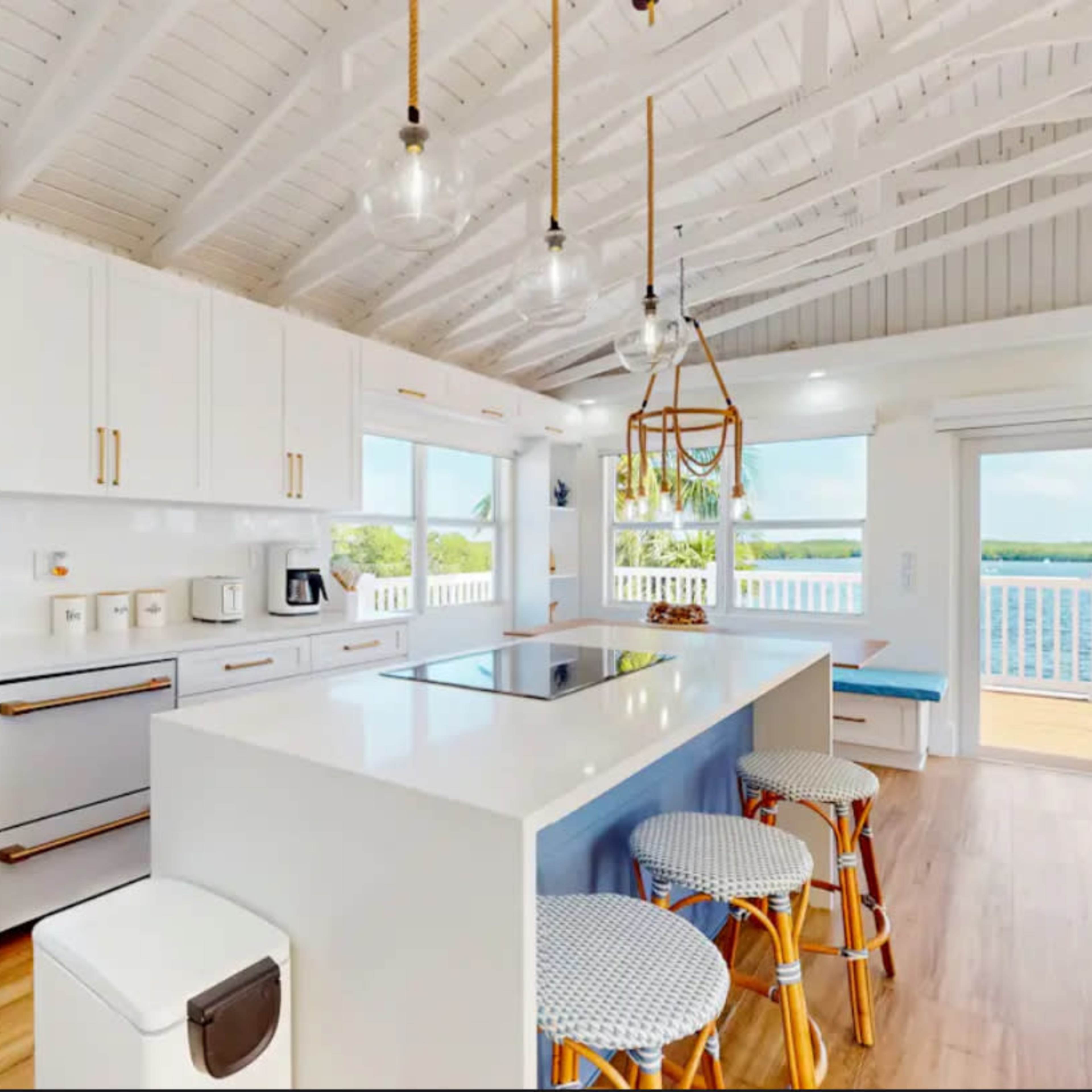 A modern kitchen features white cabinetry, a central island with a cooktop, and large windows overlooking a scenic view.