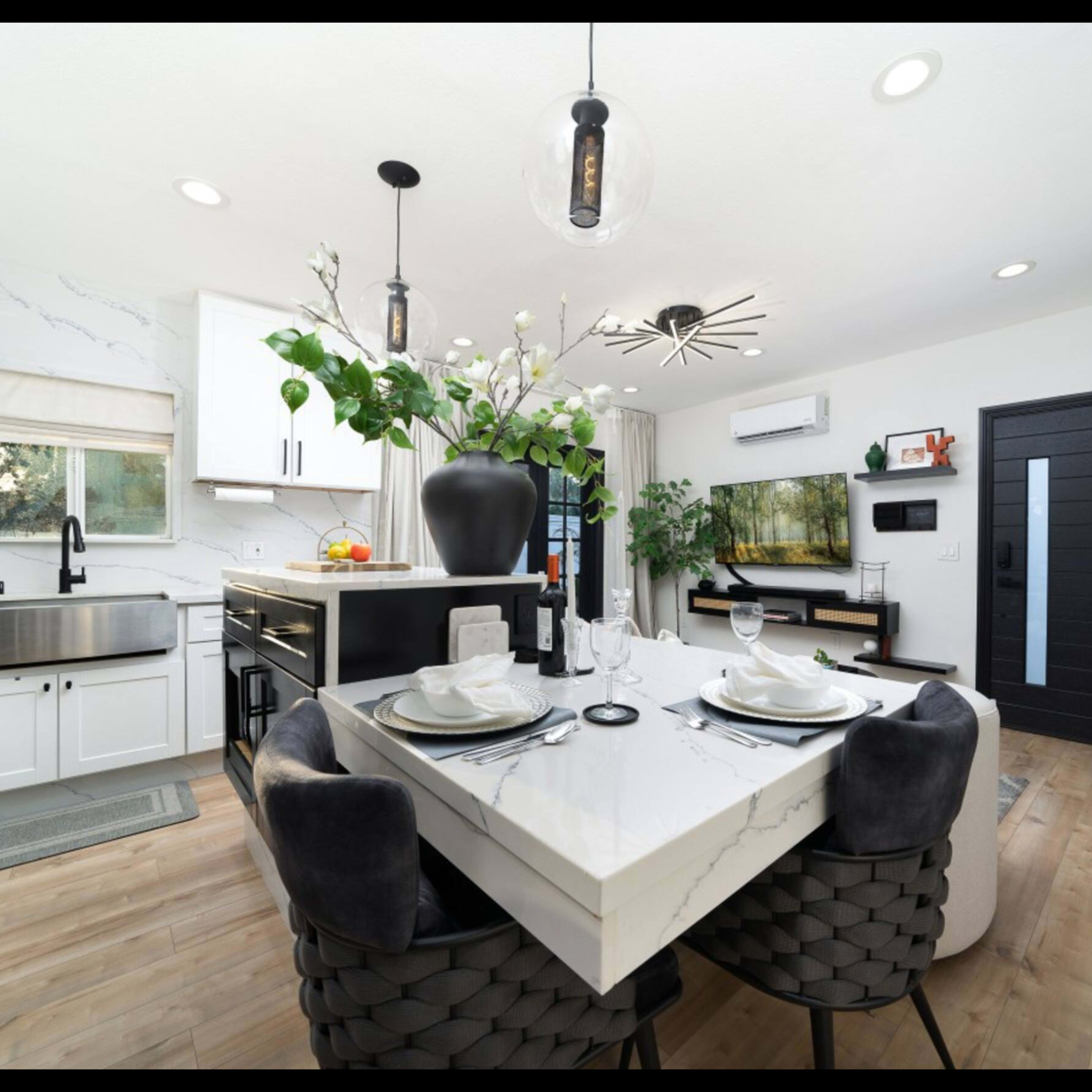 A modern kitchen and dining area features a marble table set for four, sleek cabinetry, and large windows allowing natural light.