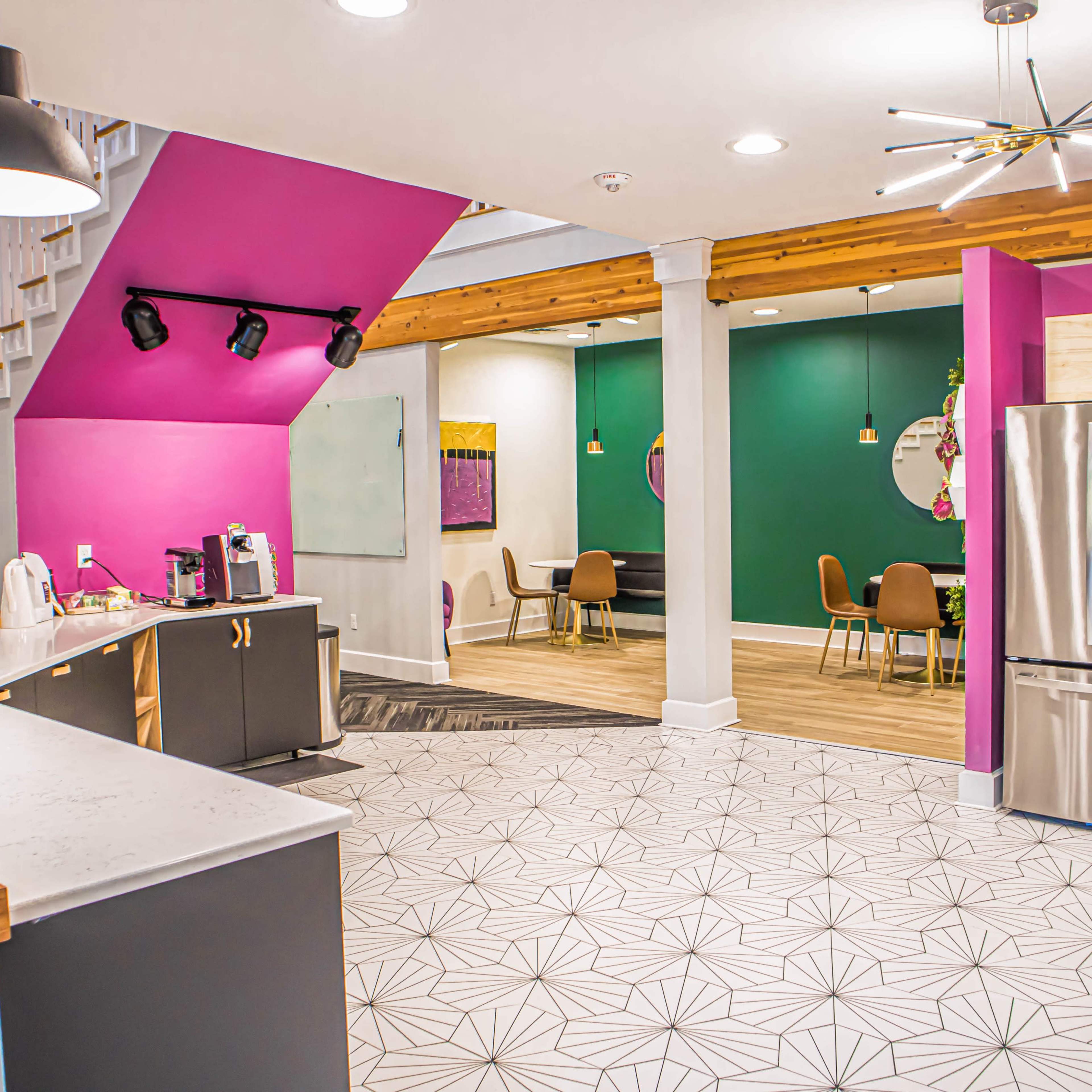 A modern open-concept space with a kitchen area featuring a stainless steel refrigerator and a seating area with chairs, walls painted in vibrant colors, and a staircase in the background.