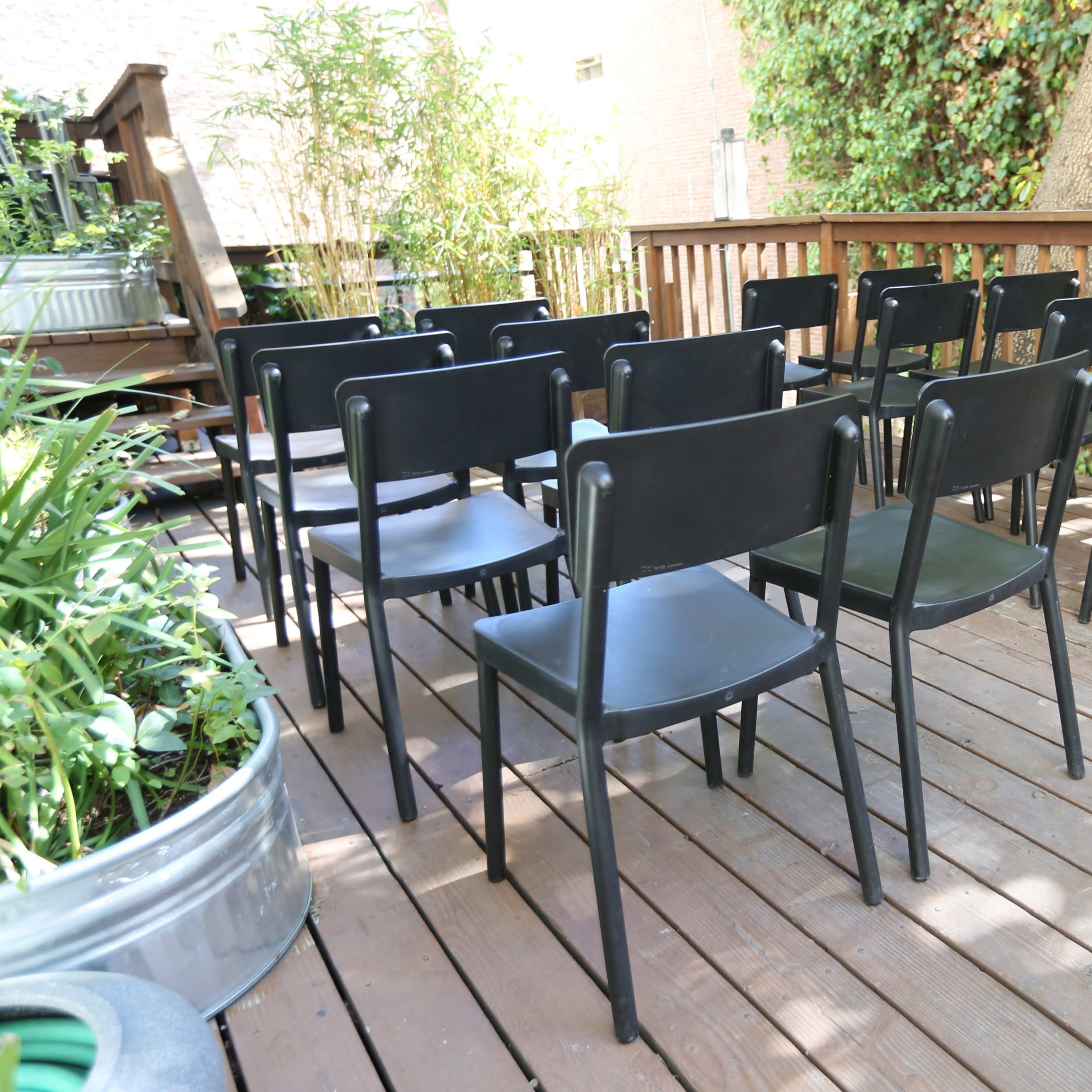 A row of black chairs is set up on a wooden deck surrounded by greenery.
