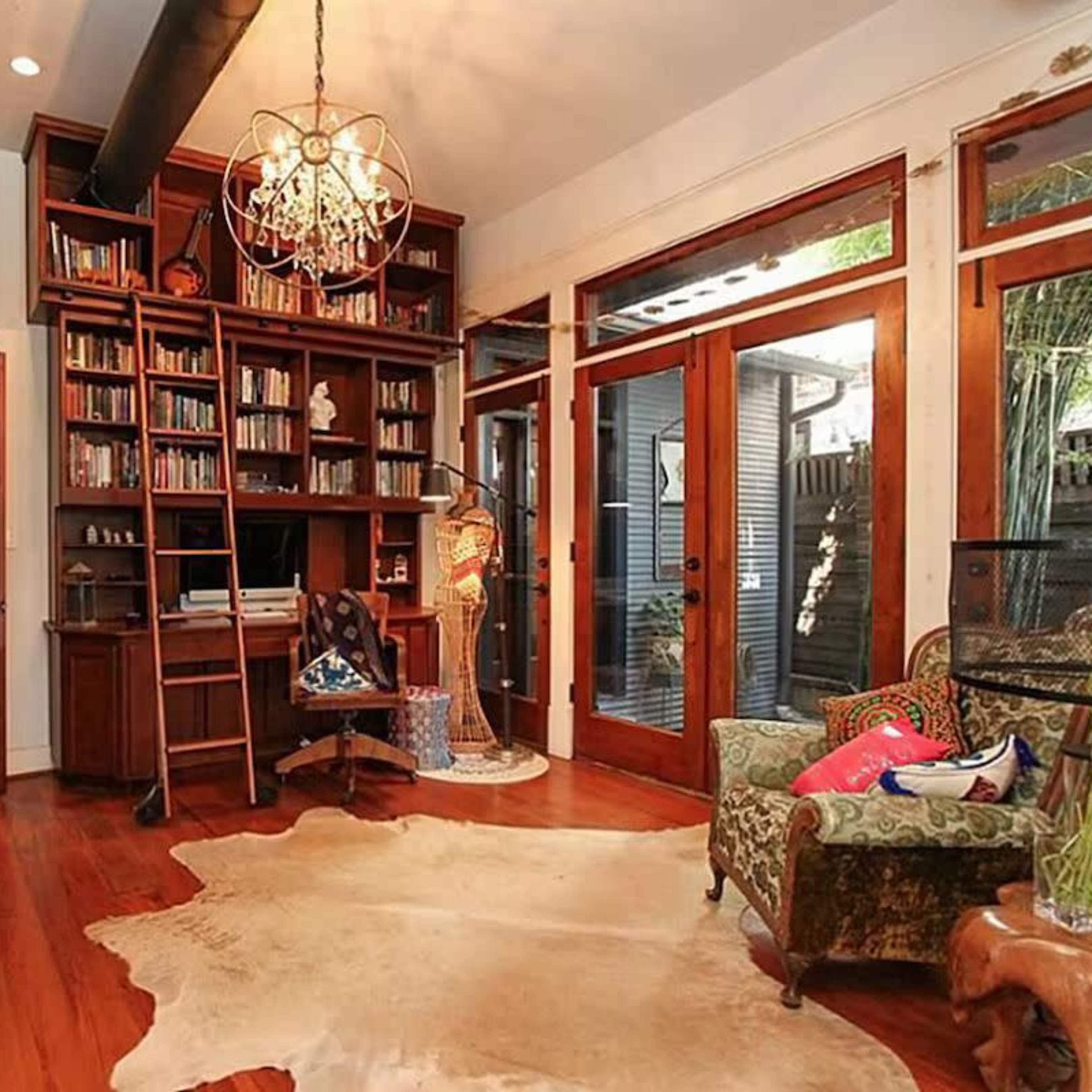 A spacious room with wooden floors, built-in bookshelves filled with books, and large glass doors that open to an outdoor area.