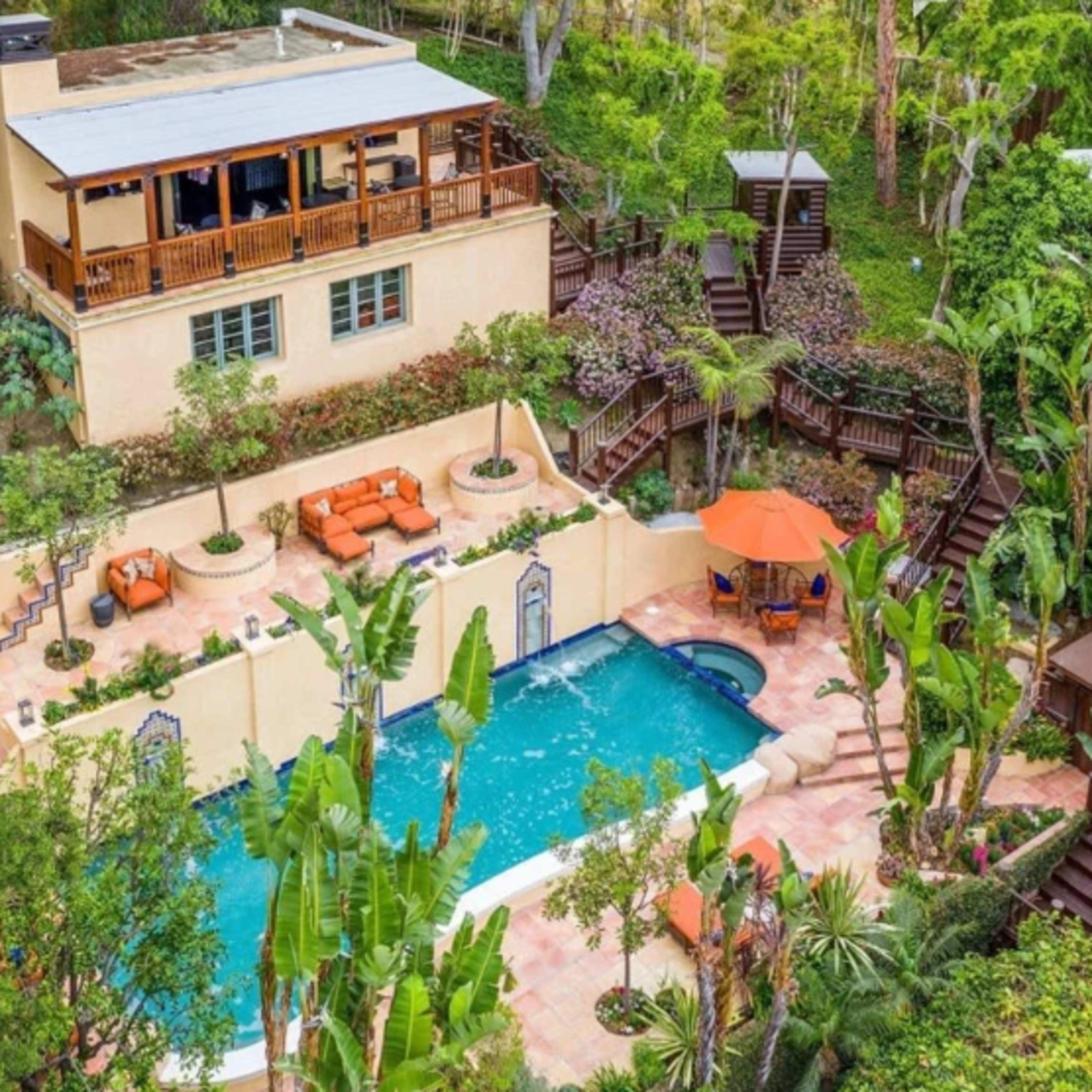 A spacious house overlooking a pool surrounded by tropical plants and lounge areas.