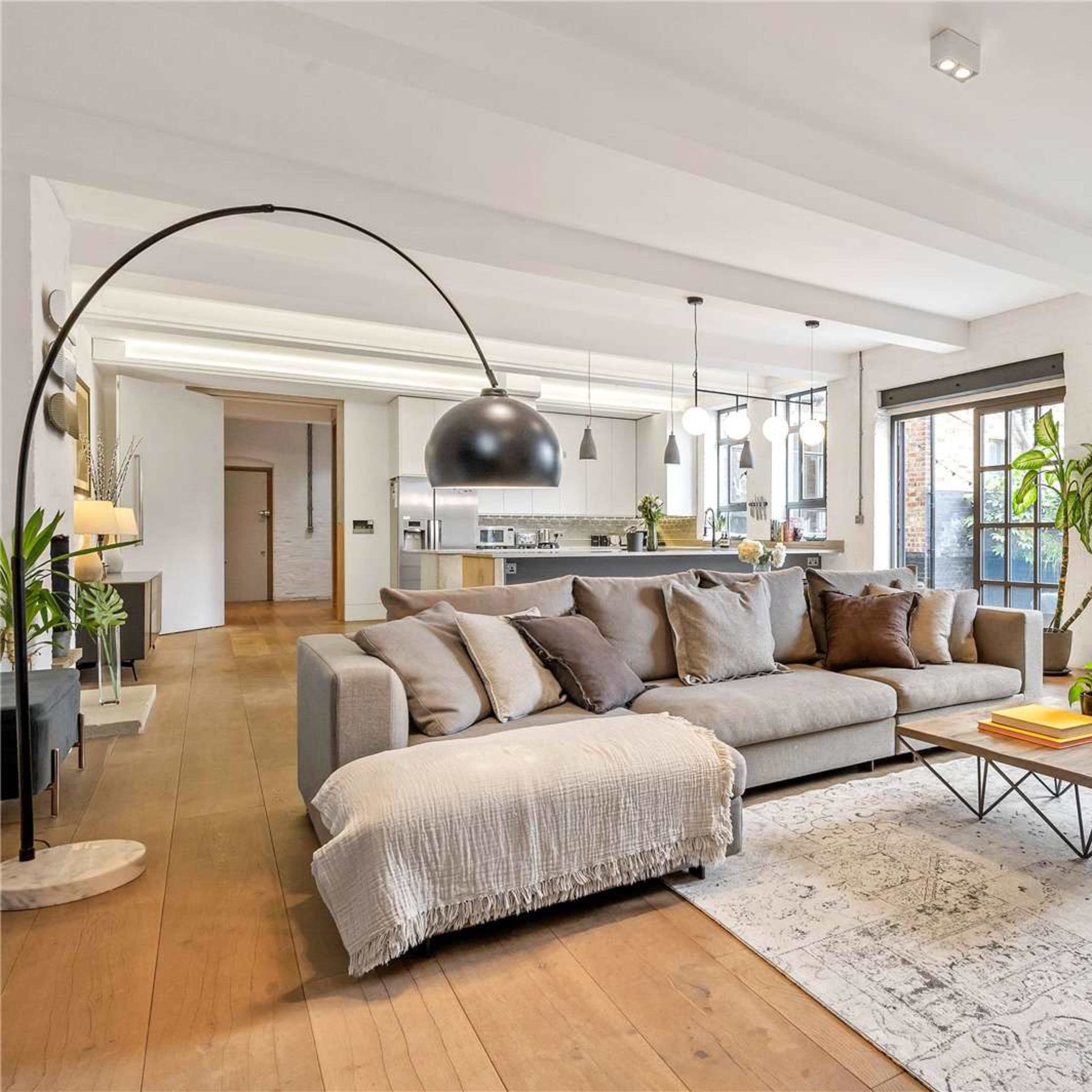 A modern living room features a large gray sofa, a coffee table, and a stylish rug, with an open kitchen visible in the background.