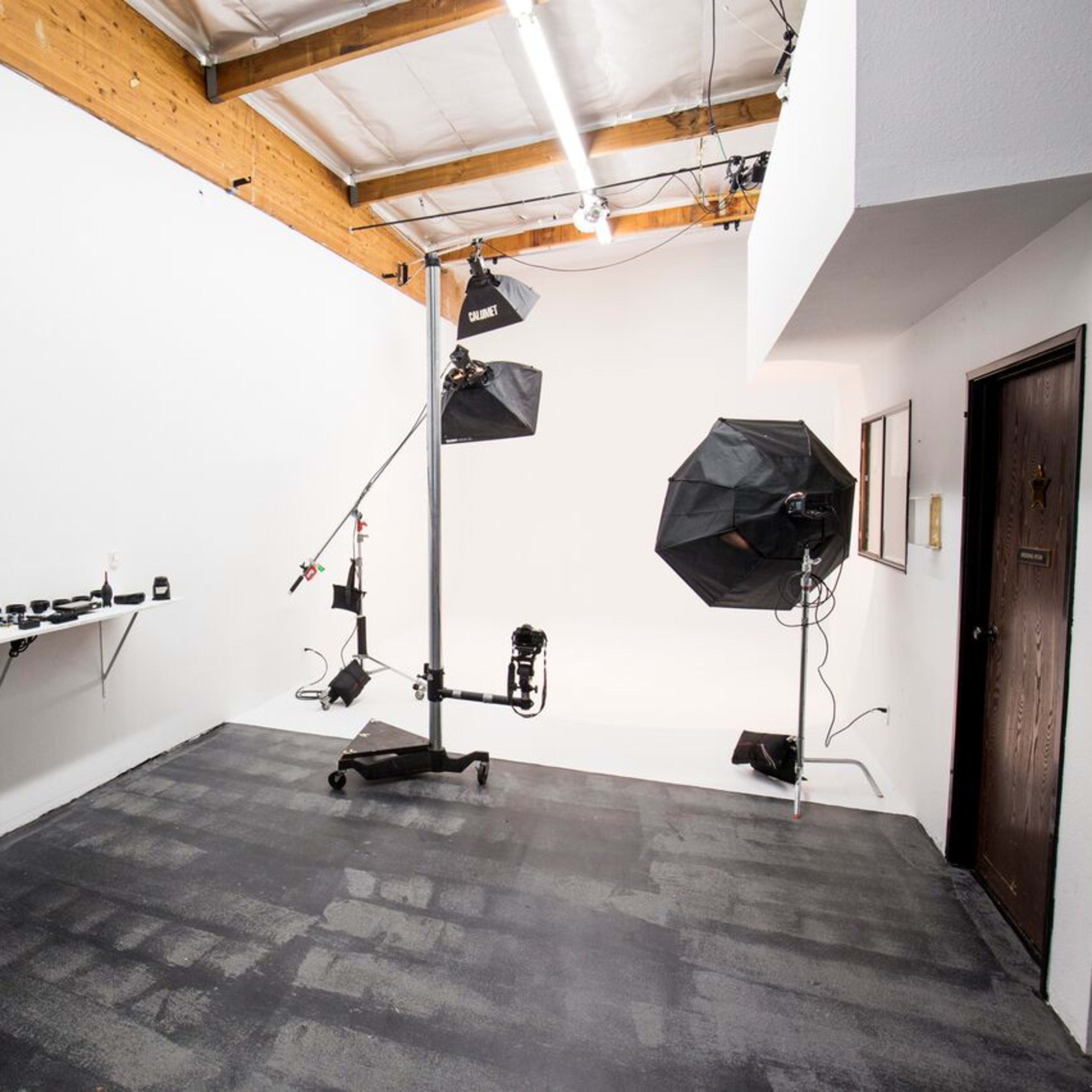 A photography studio with a variety of camera lenses on a shelf, a light stand with softboxes, and a clear, uncluttered space on the floor.