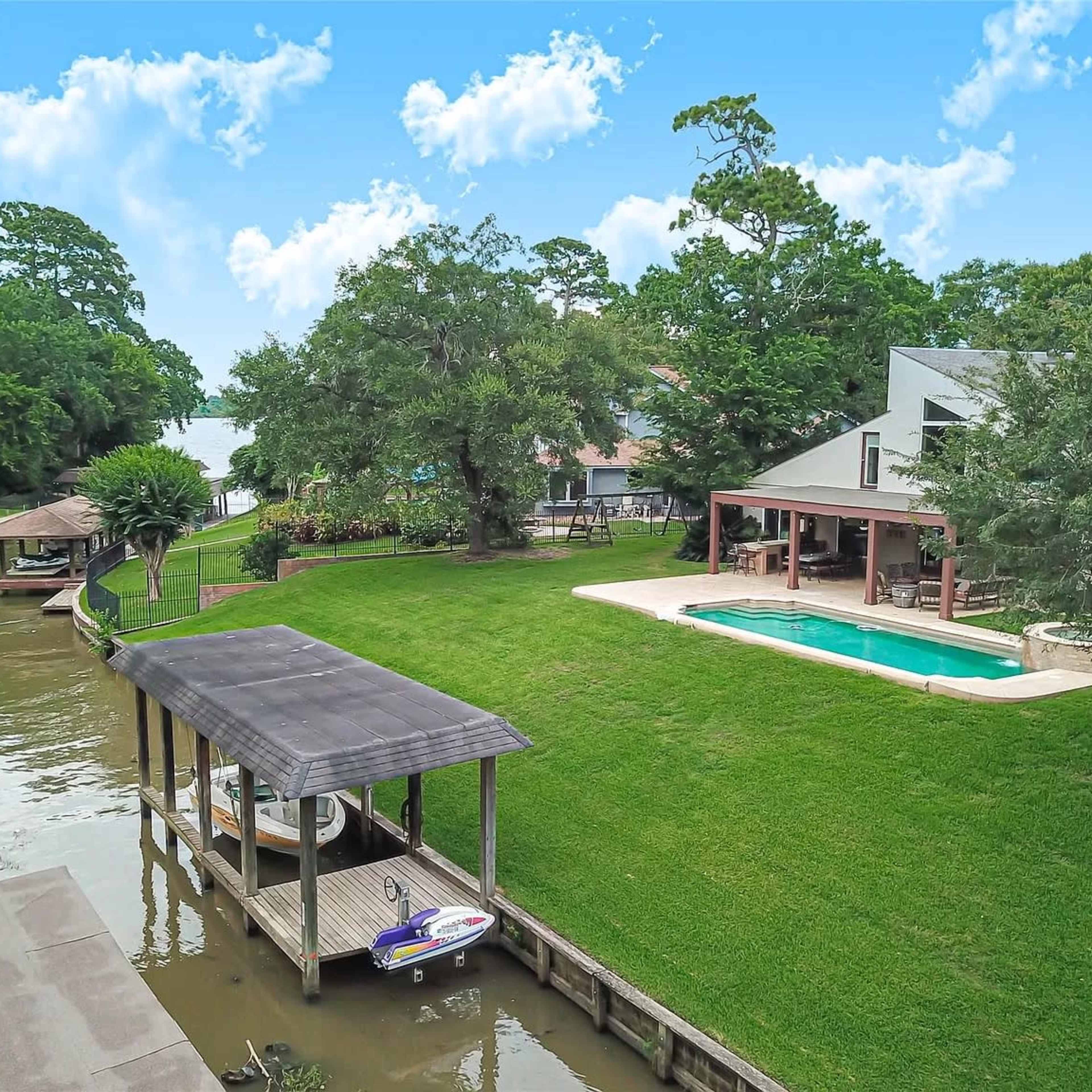 A waterfront property with a pool, dock, and a view of a lake, surrounded by lush greenery.