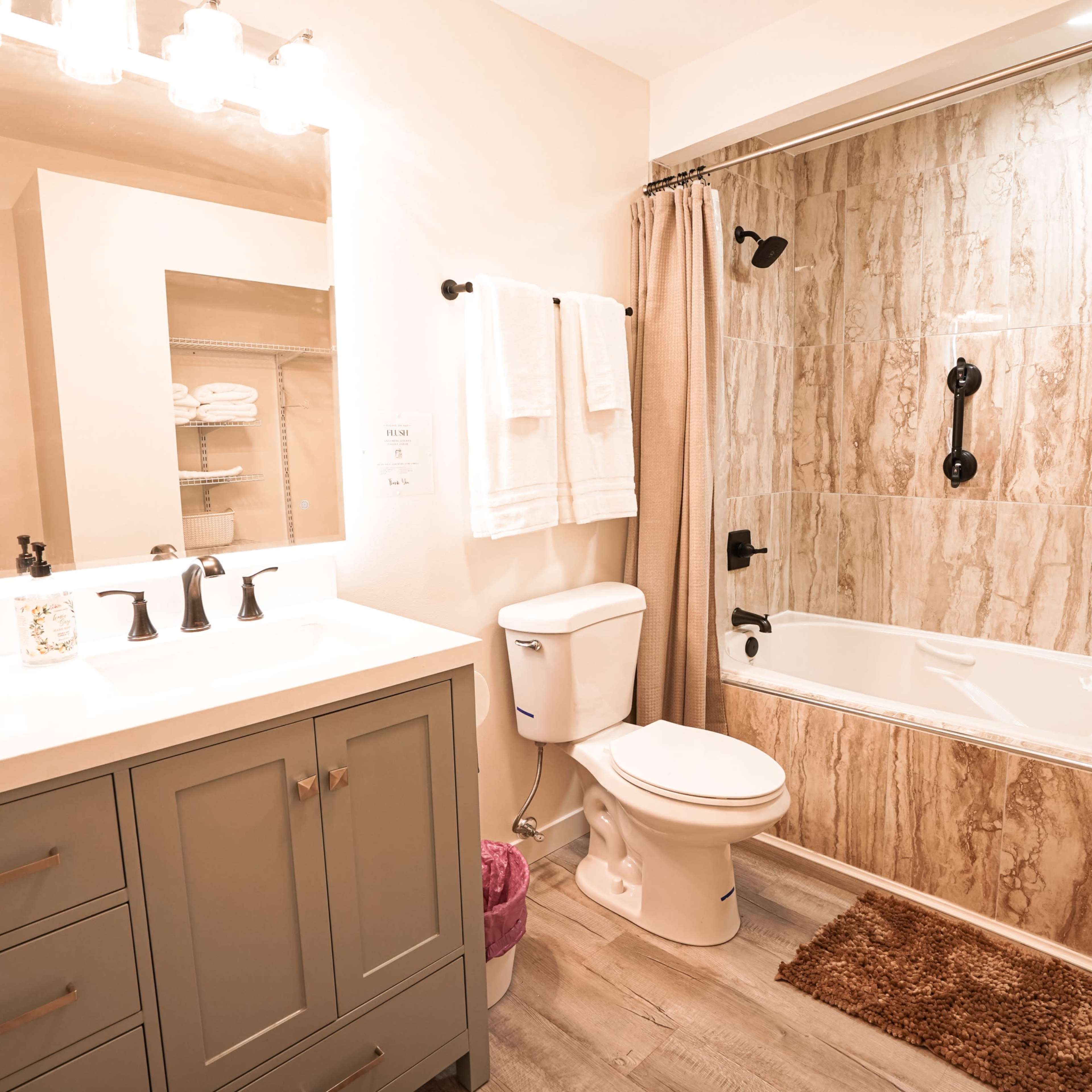 A modern bathroom featuring a bathtub with a shower, a toilet, and a vanity with a sink, all set against tiled walls and a light-colored floor.