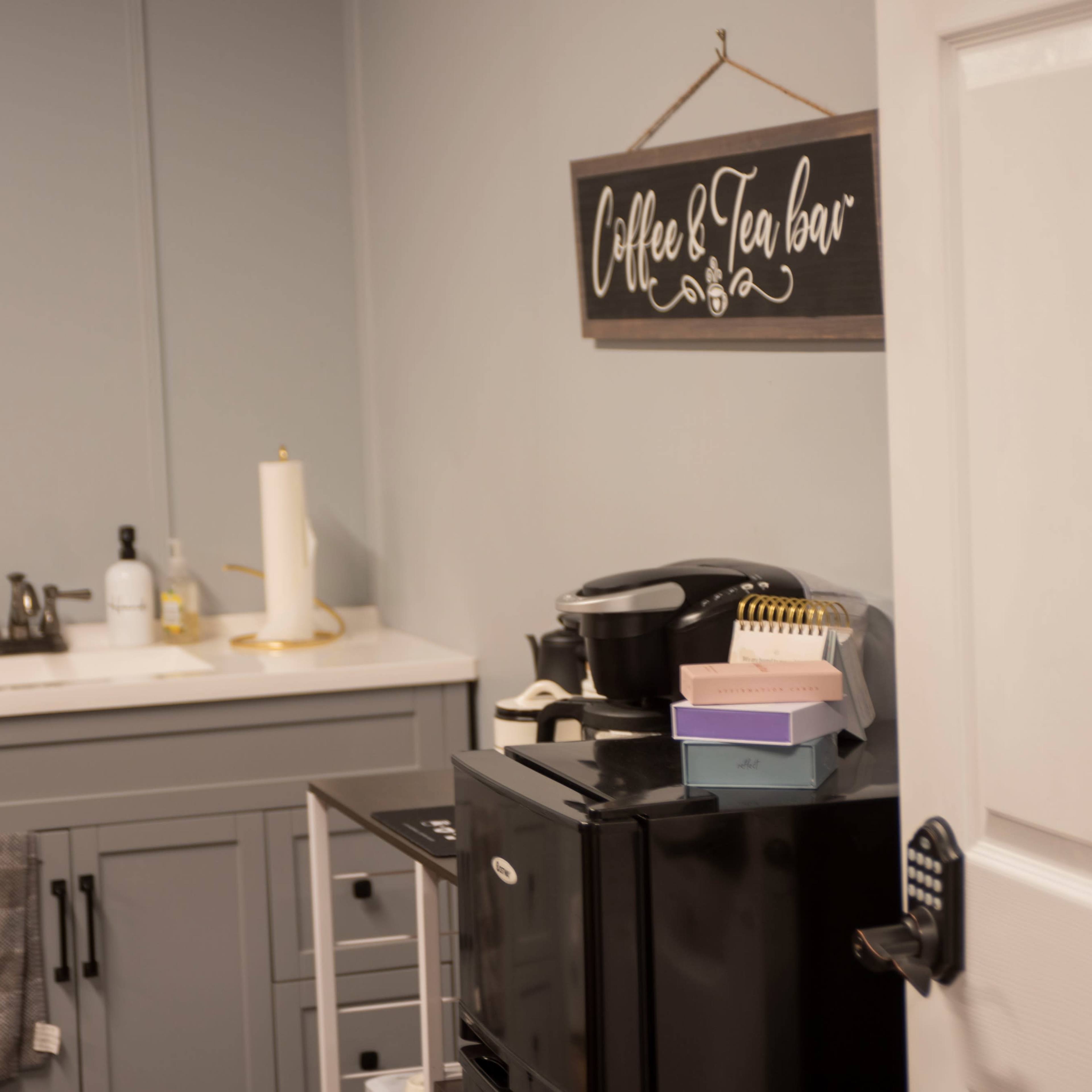 A small kitchen area with a black mini fridge, a coffee maker, and a counter featuring a dish soap dispenser and a paper towel holder.