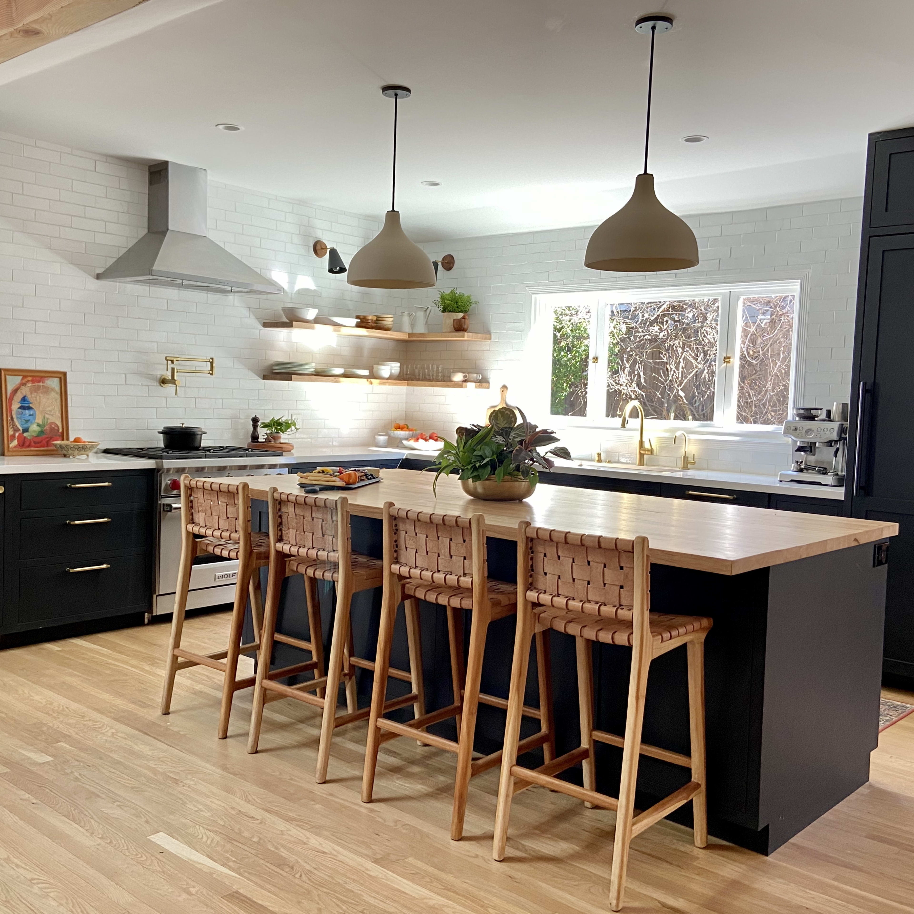 A modern kitchen features dark cabinetry, a central island with wooden seating, and a combination of pendant lighting and open shelving.
