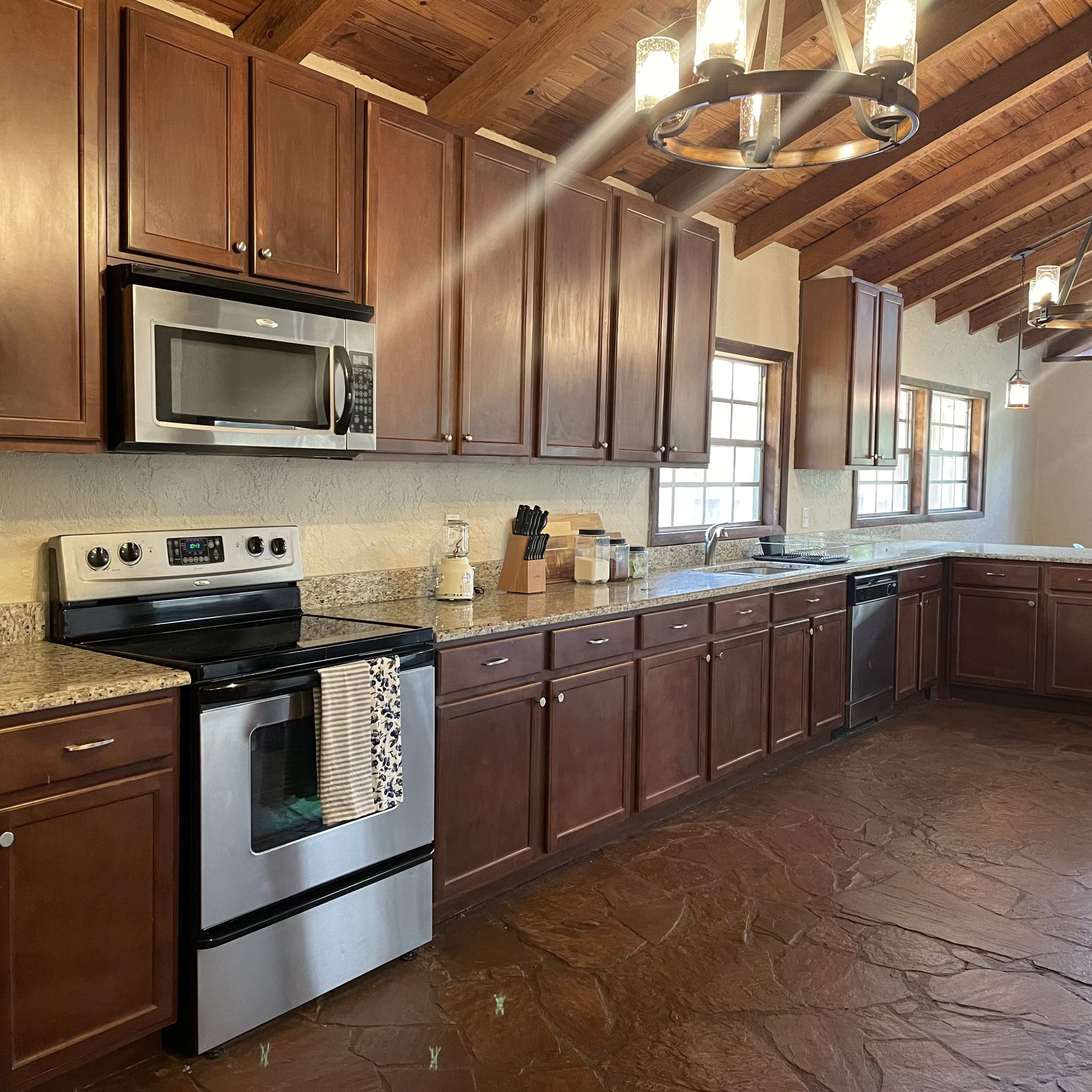 A modern kitchen with wooden cabinets, stainless steel appliances, and a high ceiling featuring exposed beams.