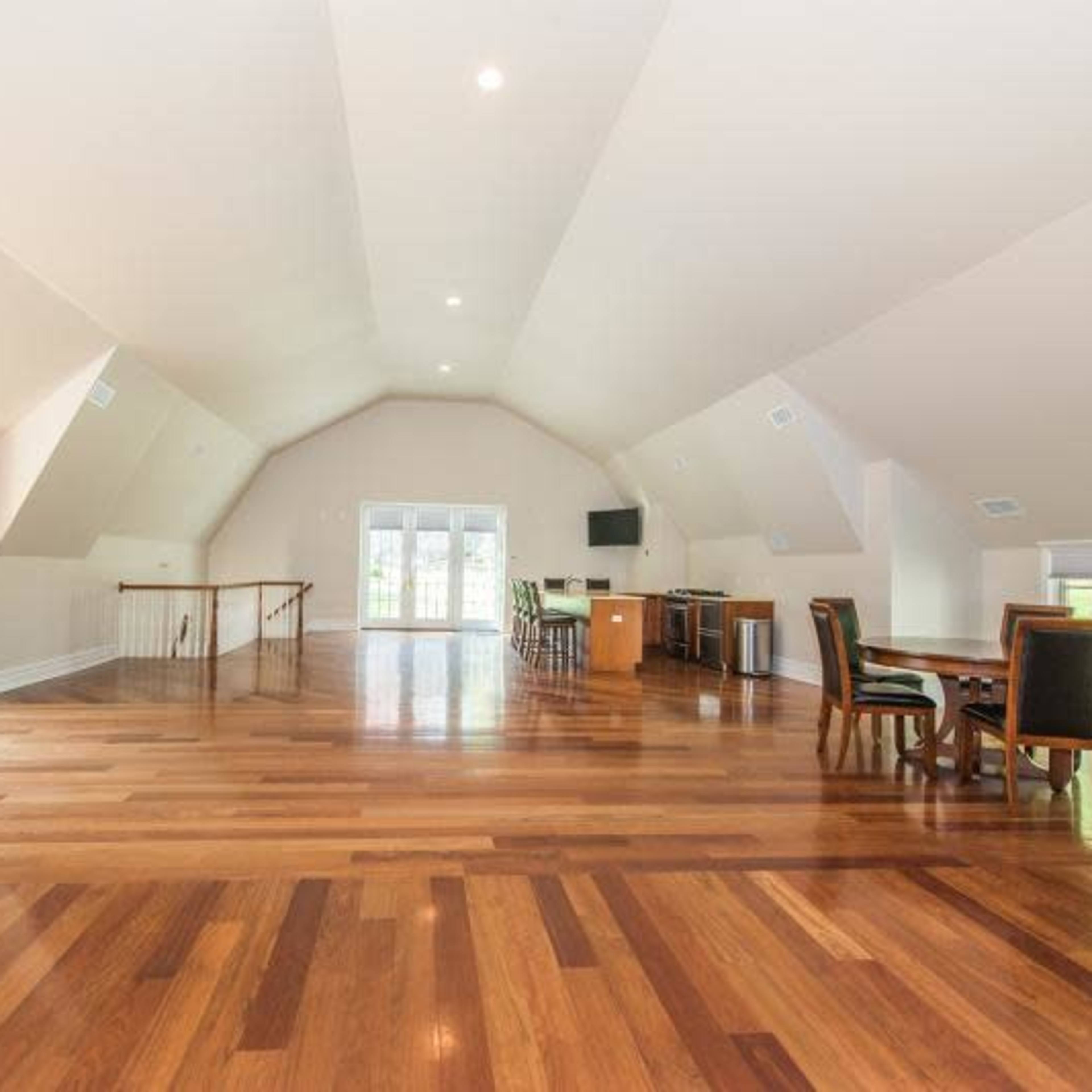 A spacious room with high ceilings, hardwood flooring, and large windows, featuring a dining area and a kitchenette.