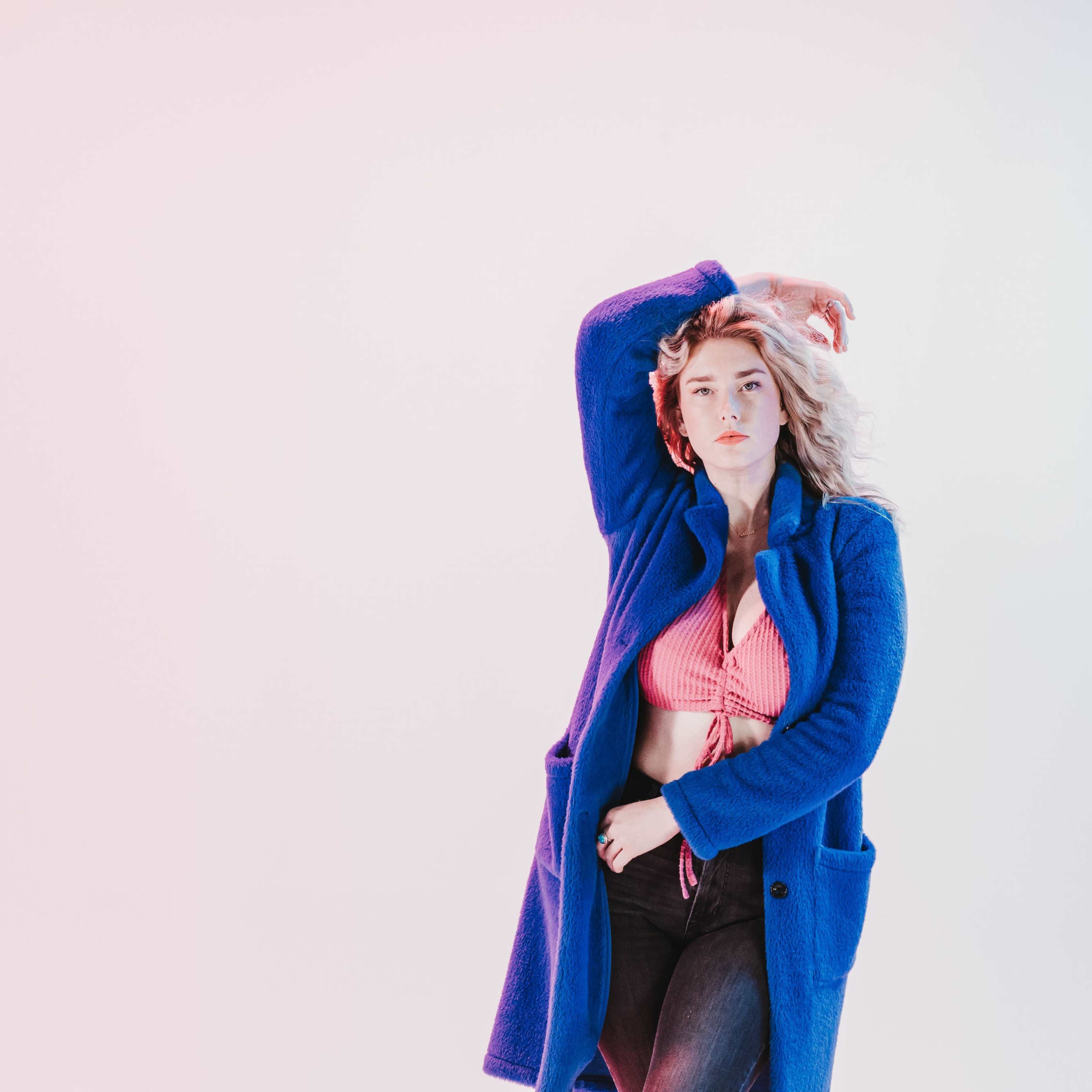 A woman wearing a blue coat and a pink top poses against a pale background.