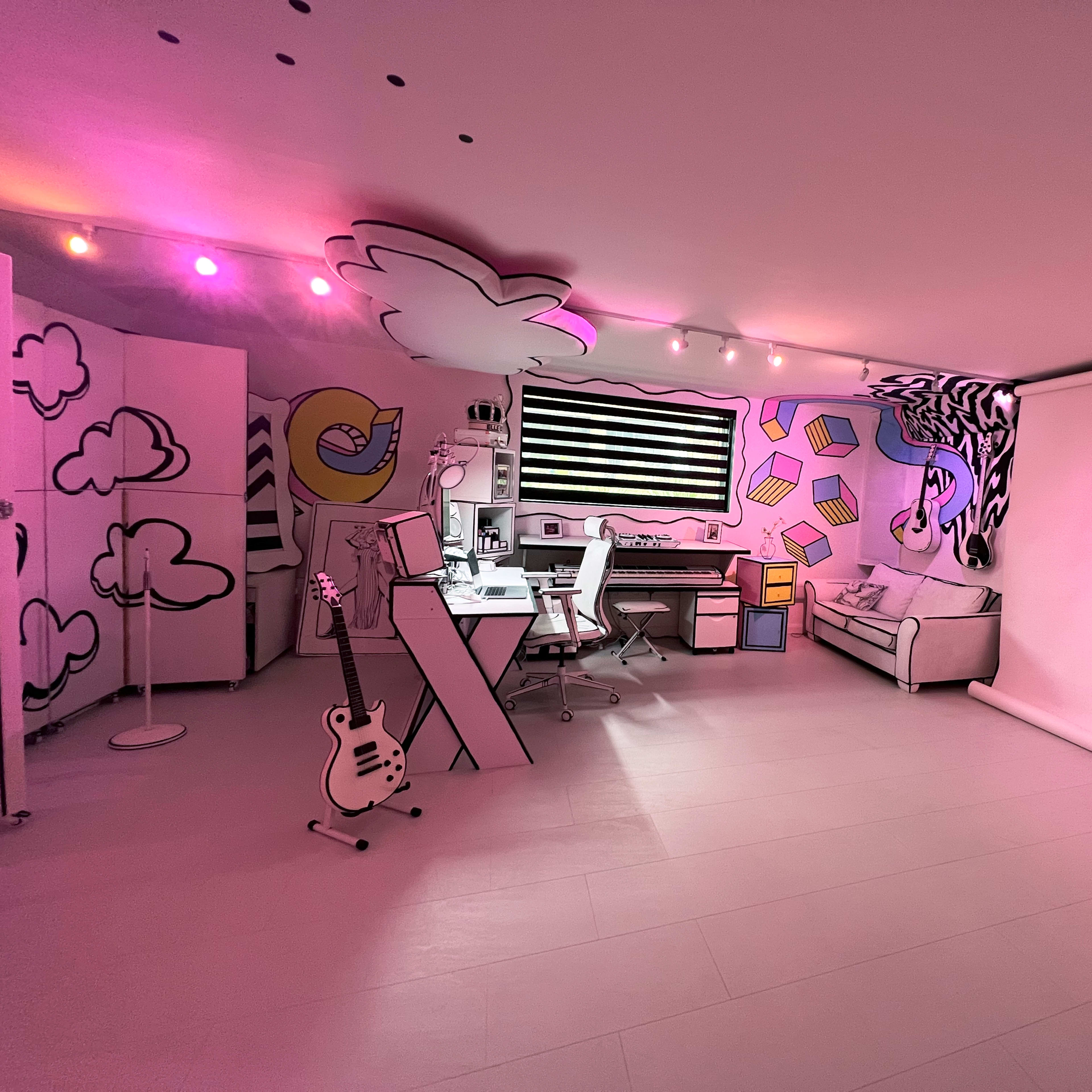 The room features a colorful, hand-drawn mural on the walls, with a workspace, a sofa, and a projector screen.