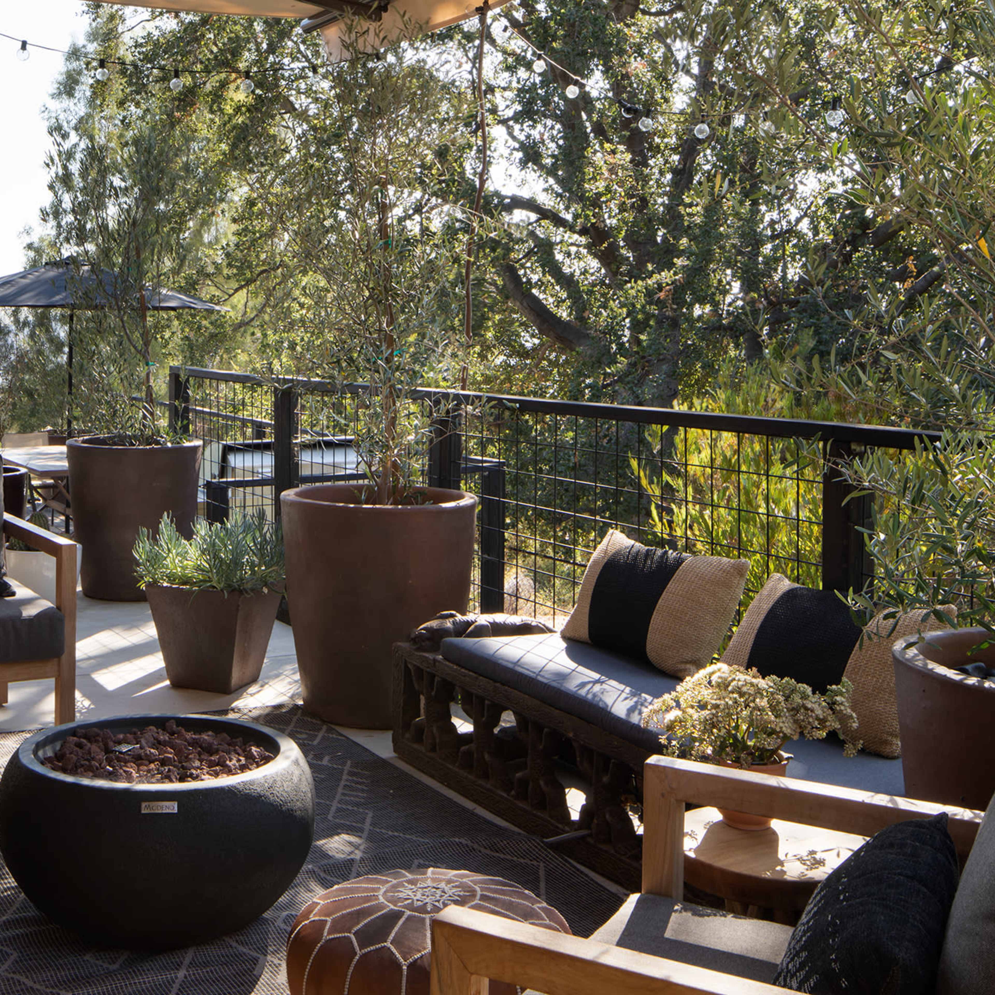 A spacious outdoor patio features comfortable seating, potted plants, and a fire pit with a view of the surrounding landscape.