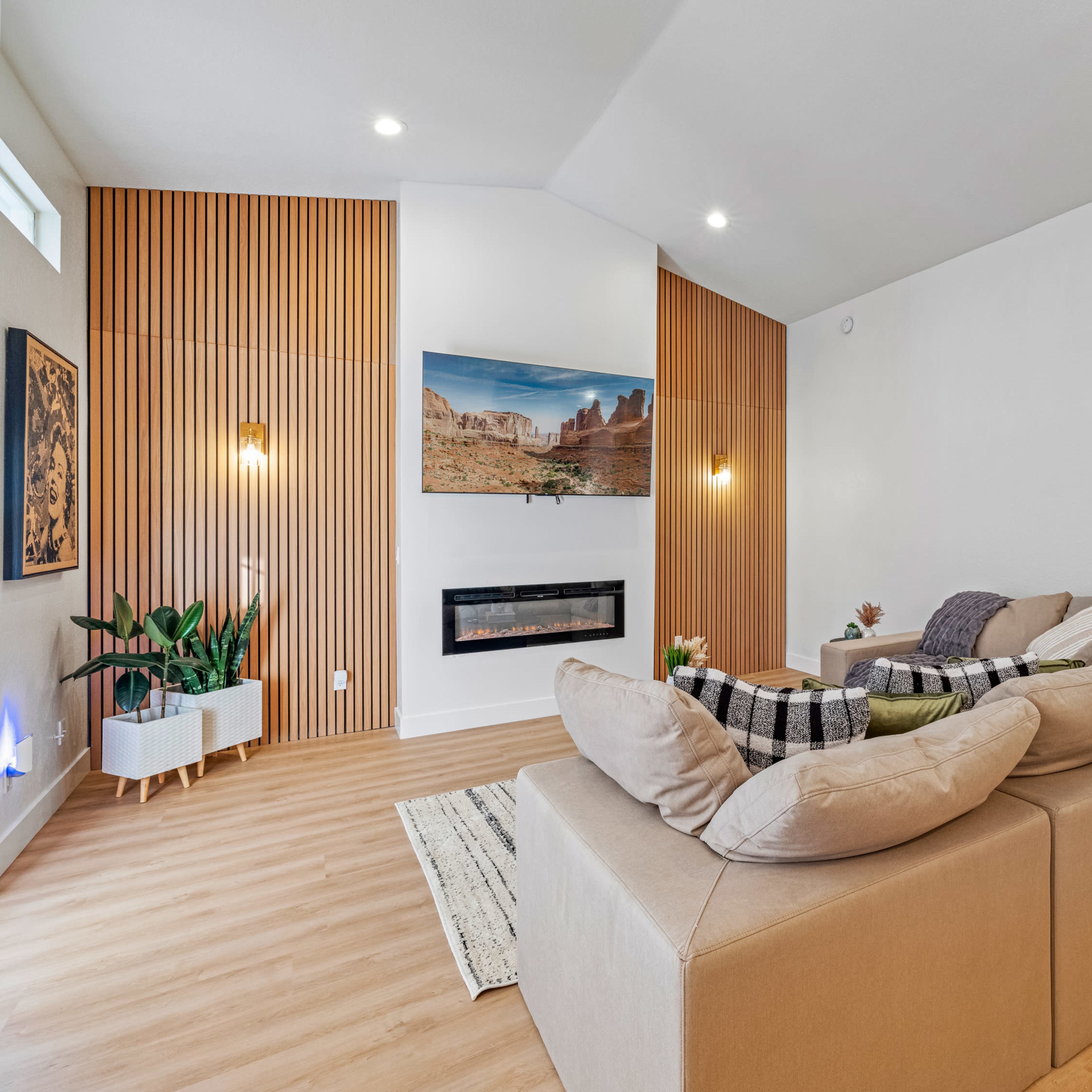 A modern living room with a sectional sofa, a mounted television, and wooden paneling on one wall.