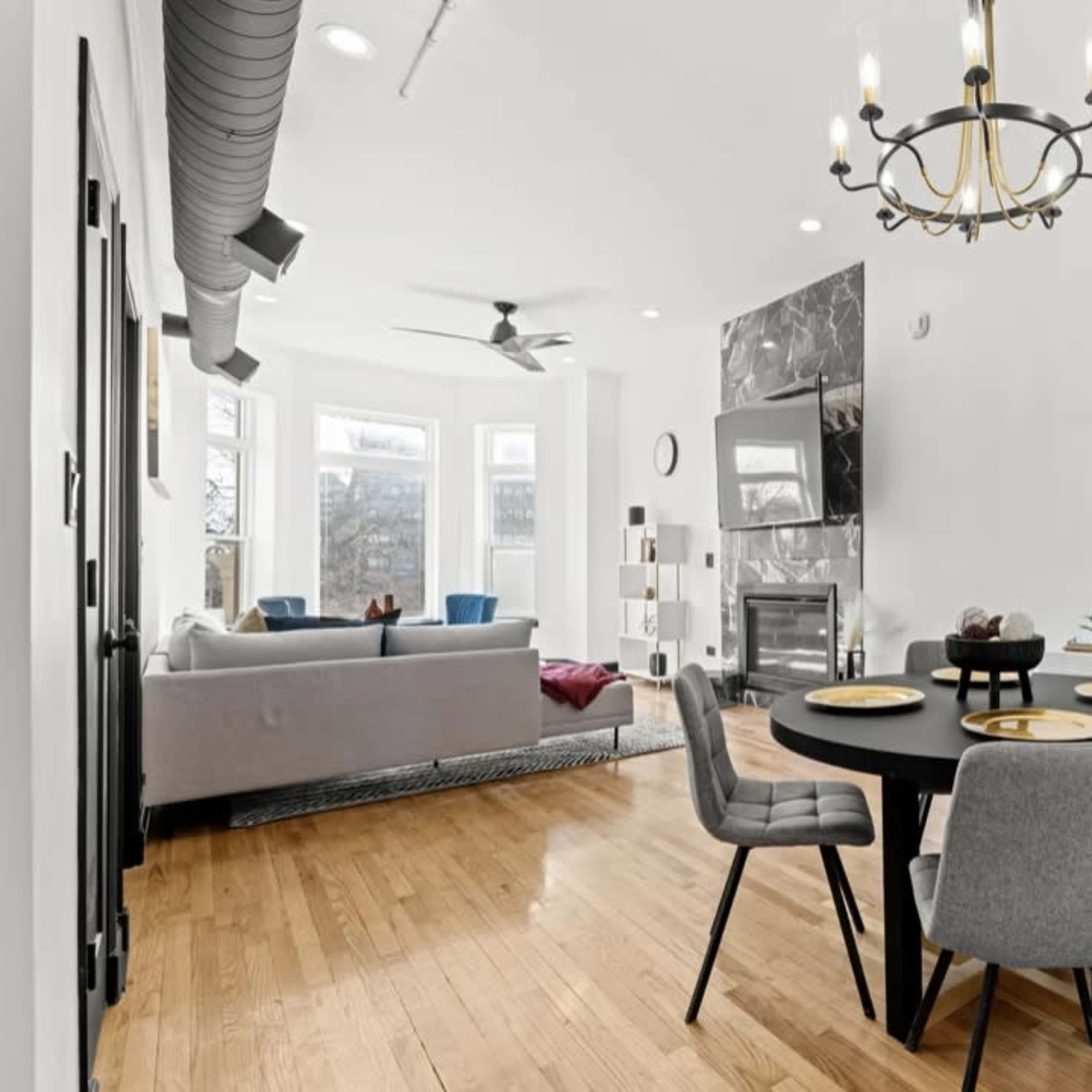 A modern dining area with a round black table and gray chairs, adjacent to a cozy living room featuring a gray sofa and a fireplace.