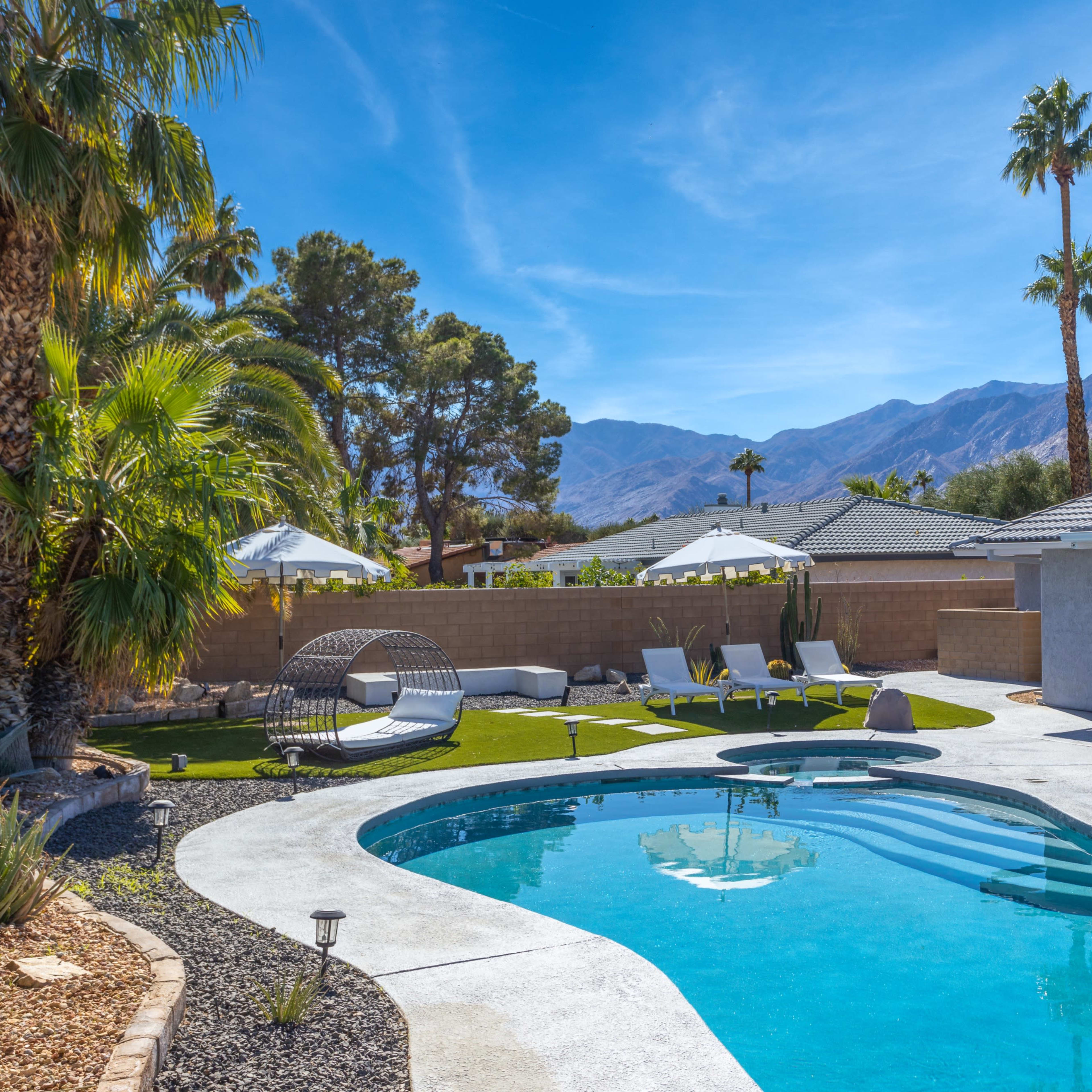 A clean swimming pool surrounded by lounge chairs, palm trees, and a mountain backdrop.