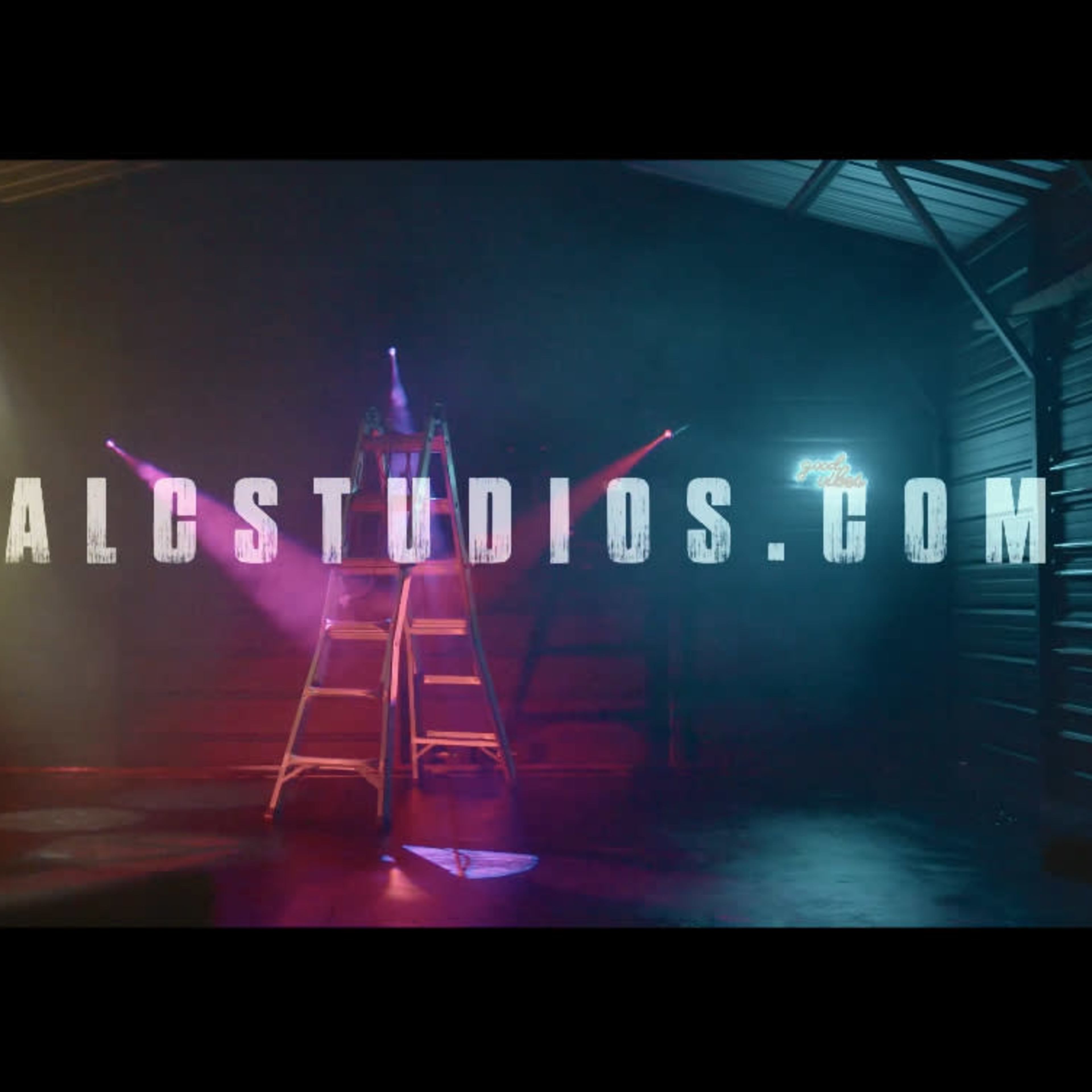 A dimly lit garage or studio space featuring a ladder and illuminated signs casting colored lights.