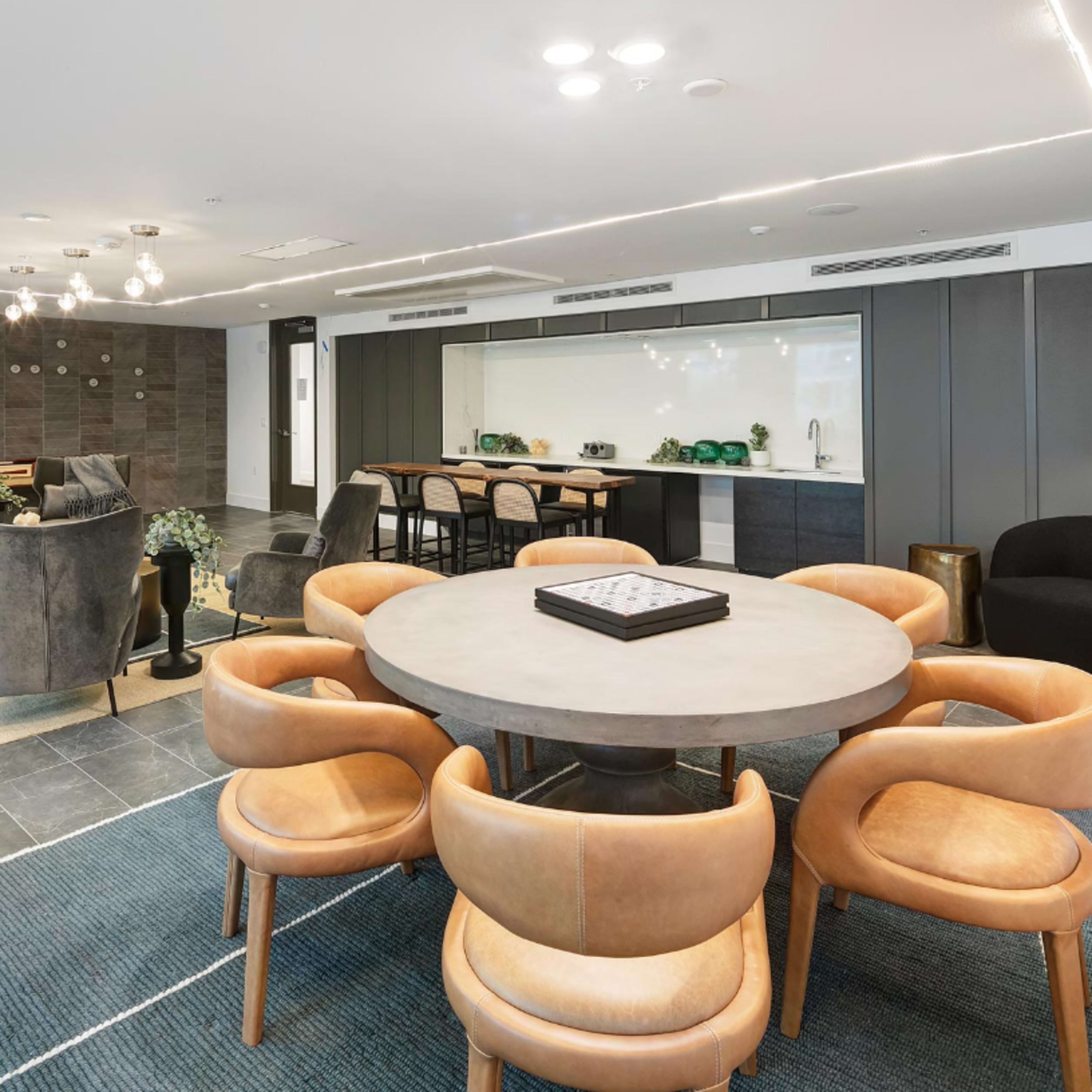 A modern dining area with a round table surrounded by upholstered chairs and a sleek kitchen in the background.